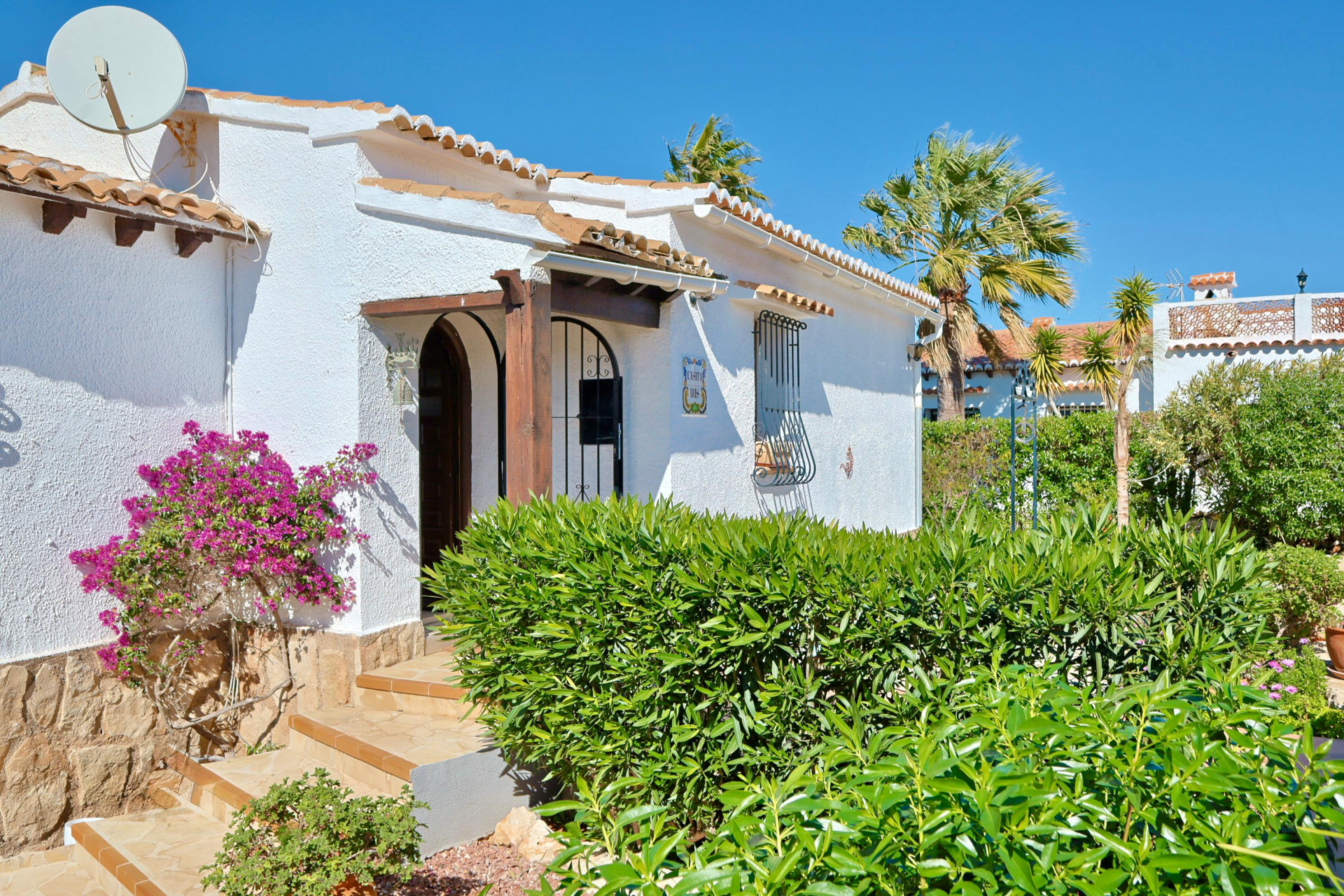Fachada de villa mediterránea con buganvilla y entrada con arco de madera.