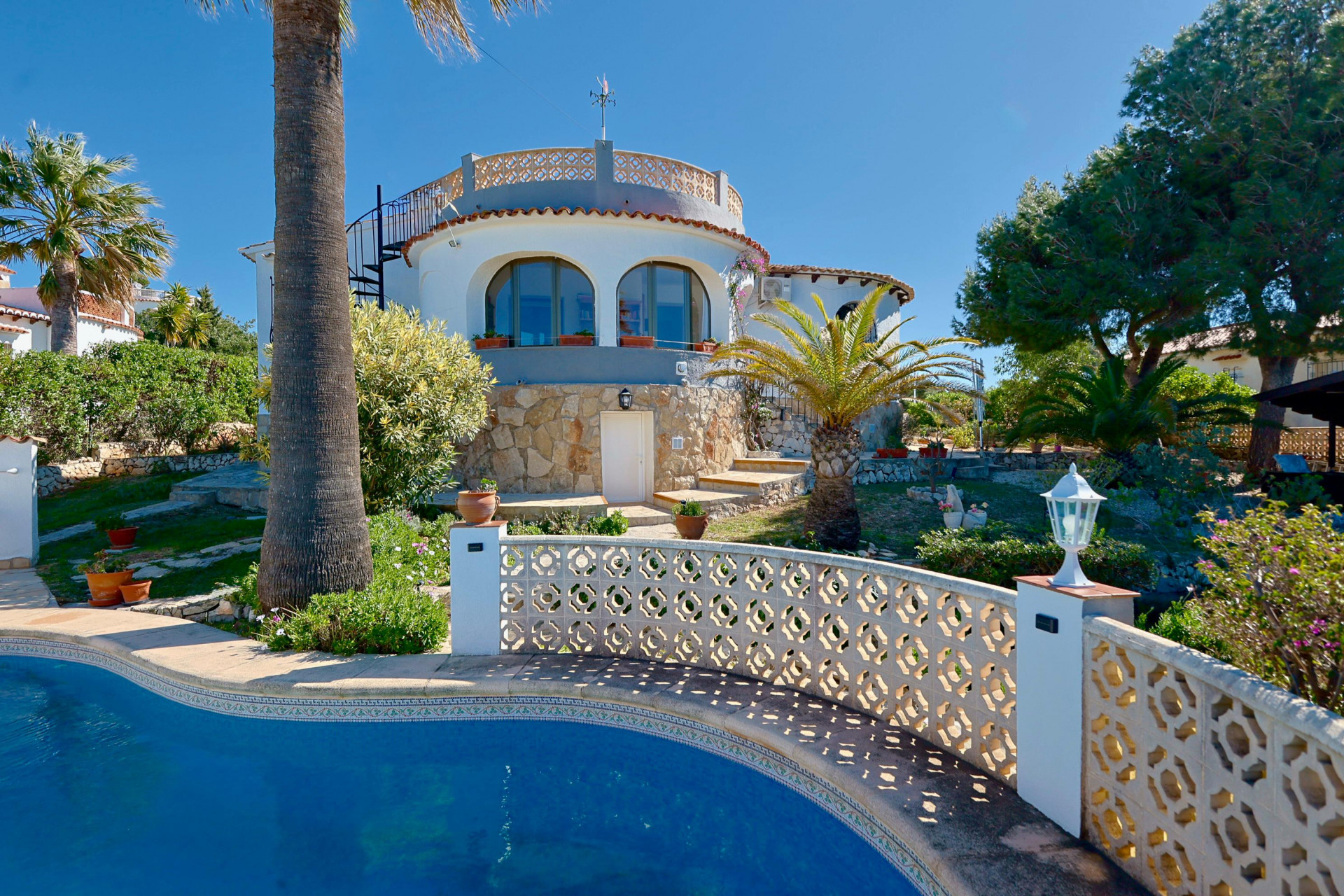 Vista de la piscina con barandilla de celosía y la fachada de piedra de la villa en Jávea.