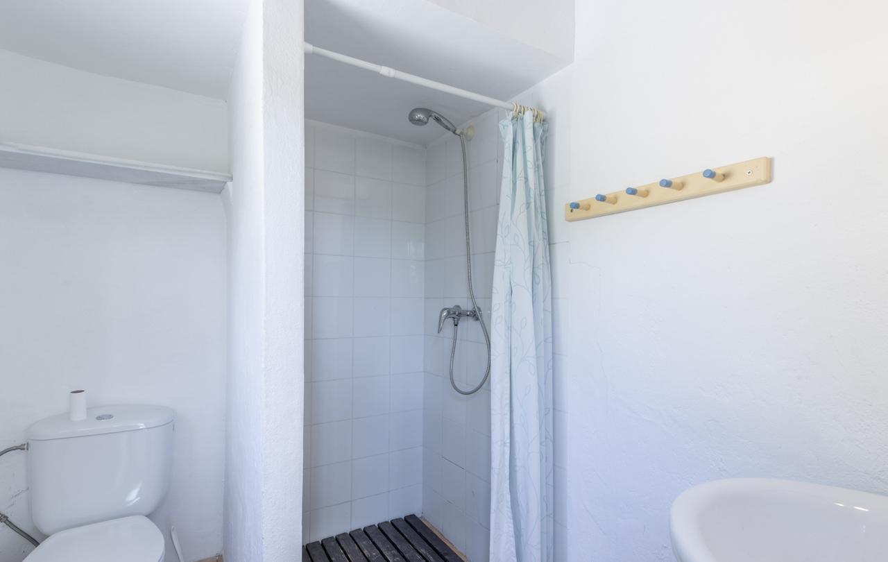 Baño funcional con ducha de azulejos blancos, suelo de tarima de madera oscura, cortina estampada y perchero de madera con pomos azules.