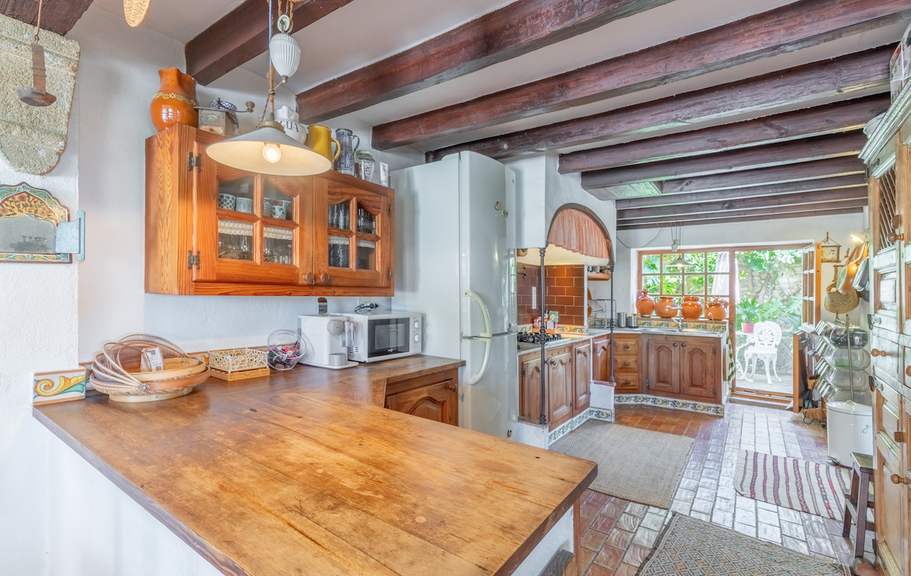 Cocina de estilo tradicional valenciano con vigas de madera vista, encimeras de madera maciza y acceso directo a un patio exterior ajardinado.