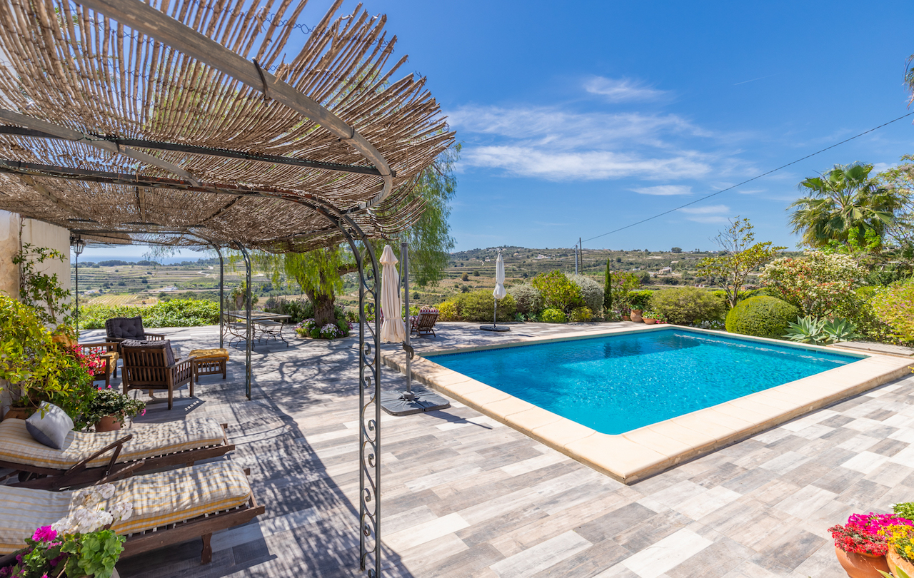Terraza exterior con piscina y pérgola de forja con techado de cañizo. Ofrece vistas panorámicas al valle y pavimentos antideslizantes rodeados de vegetación mediterránea.