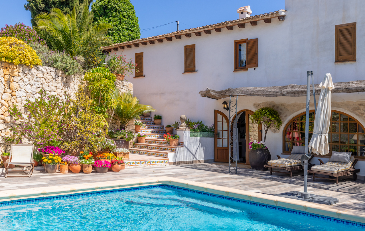 Zona de piscina con amplia terraza antideslizante, fachada blanca con contraventanas de madera y escaleras exteriores decoradas con azulejos cerámicos tradicionales.