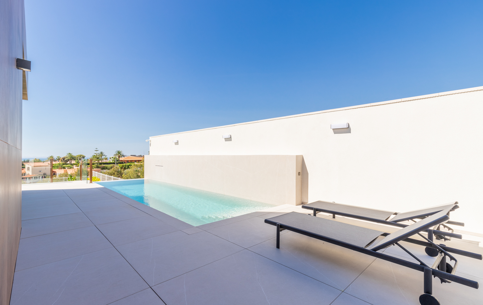 Detalle de la piscina infinita con vistas y tumbonas sobre baldosa gris.