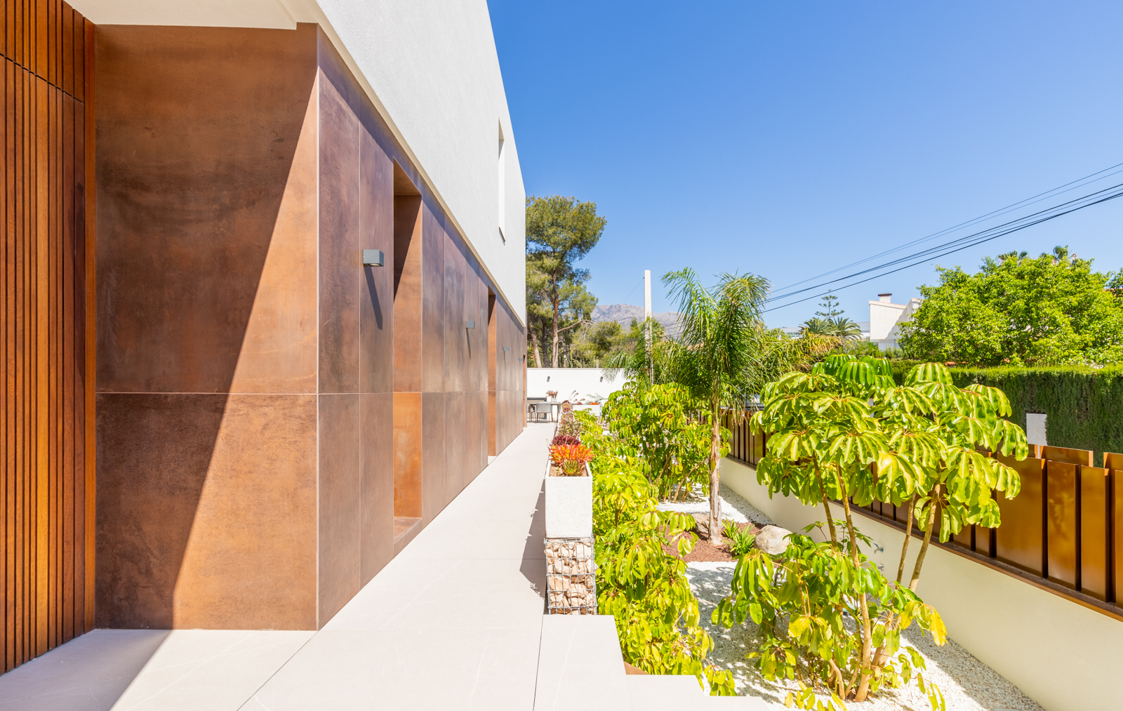 Vista exterior de la villa con jardín mediterráneo y pared revestida en tonos tierra.