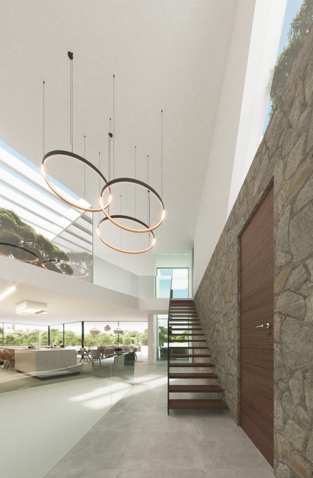 Hall de entrada de doble altura con pared de piedra natural, escalera volada de madera y modernas lámparas circulares bajo un gran lucernario que aporta luz cenital.