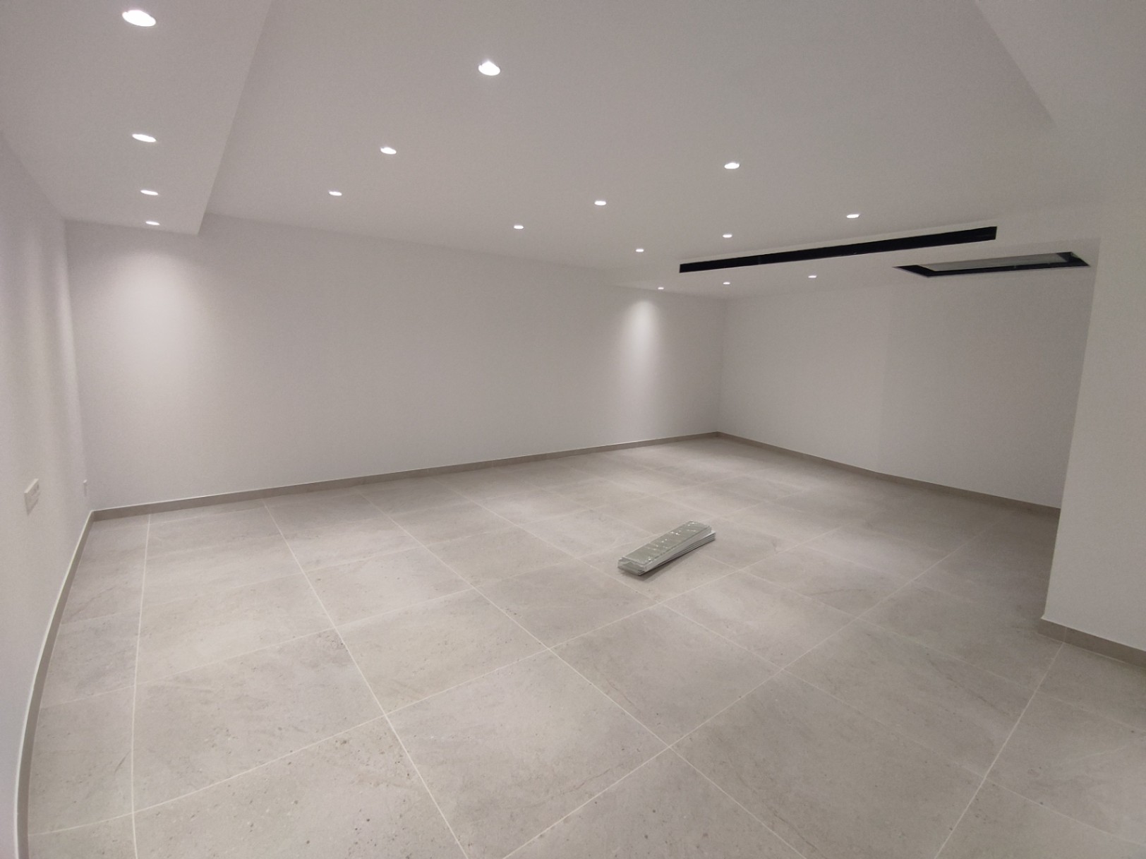 Amplia sala diáfana con suelos de gres porcelánico de gran formato, paredes blancas y un sistema de iluminación mediante focos LED empotrados en el techo.
