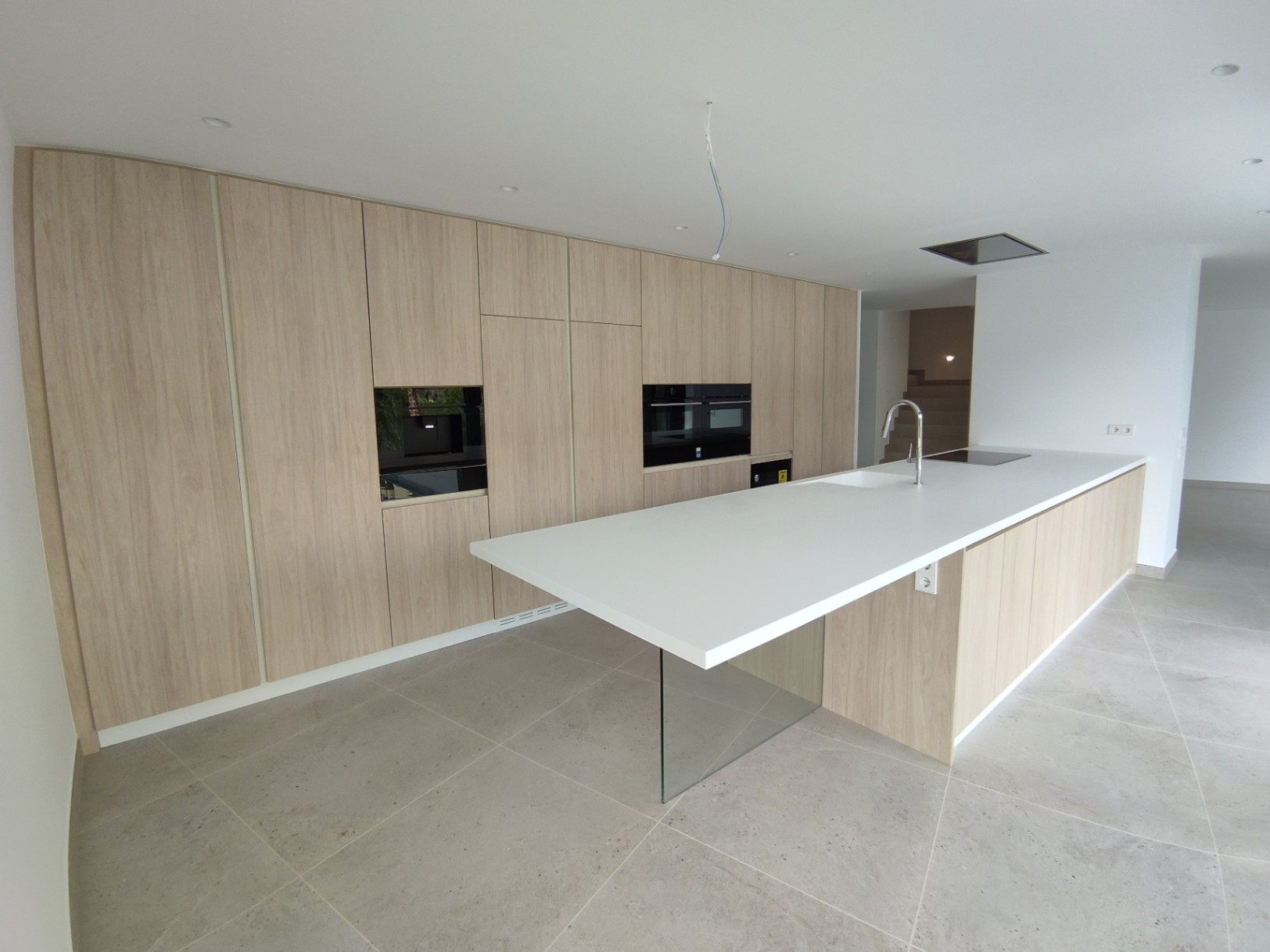 Cocina de diseño con armarios de madera, electrodomésticos integrados y una isla blanca minimalista apoyada sobre una base de cristal transparente.