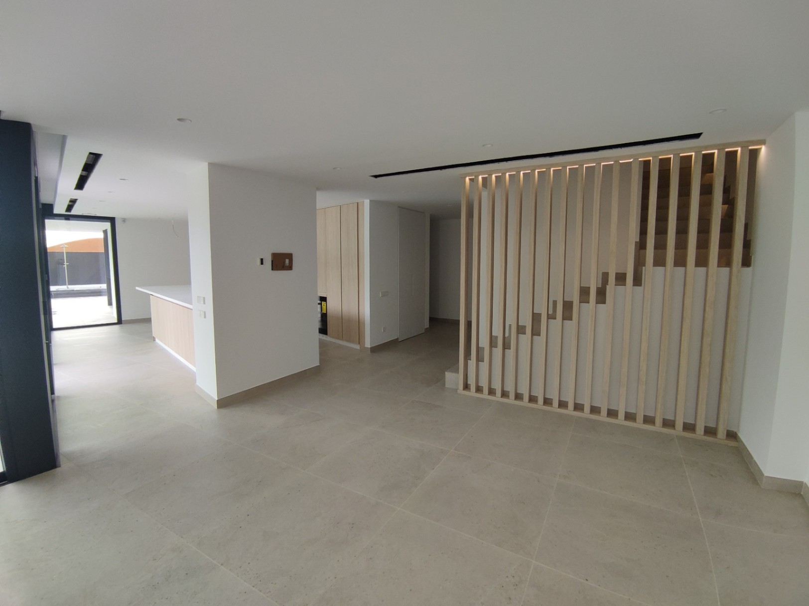 Distribución de planta abierta con suelos porcelánicos, destacando la escalera de diseño con lamas verticales de madera y retroiluminación LED.