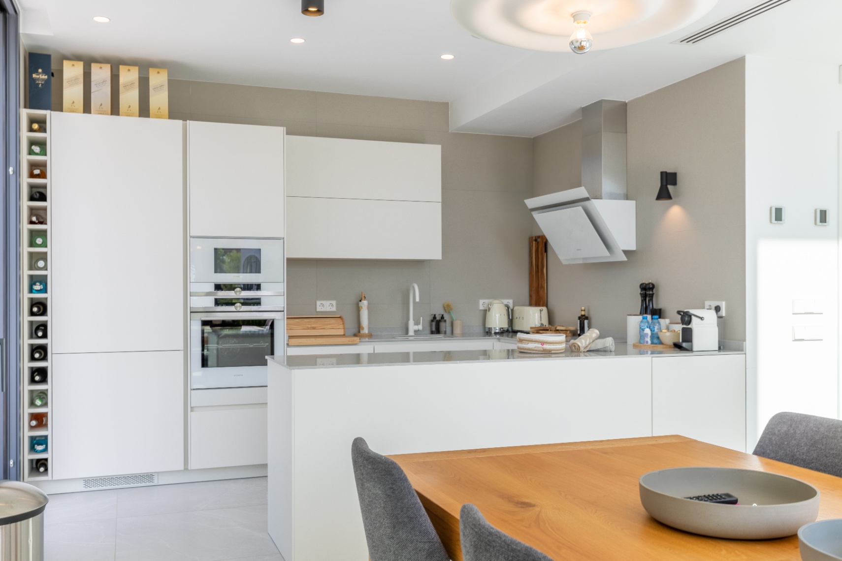 Cocina moderna con armarios blancos, electrodomésticos integrados y mesa de comedor de madera.