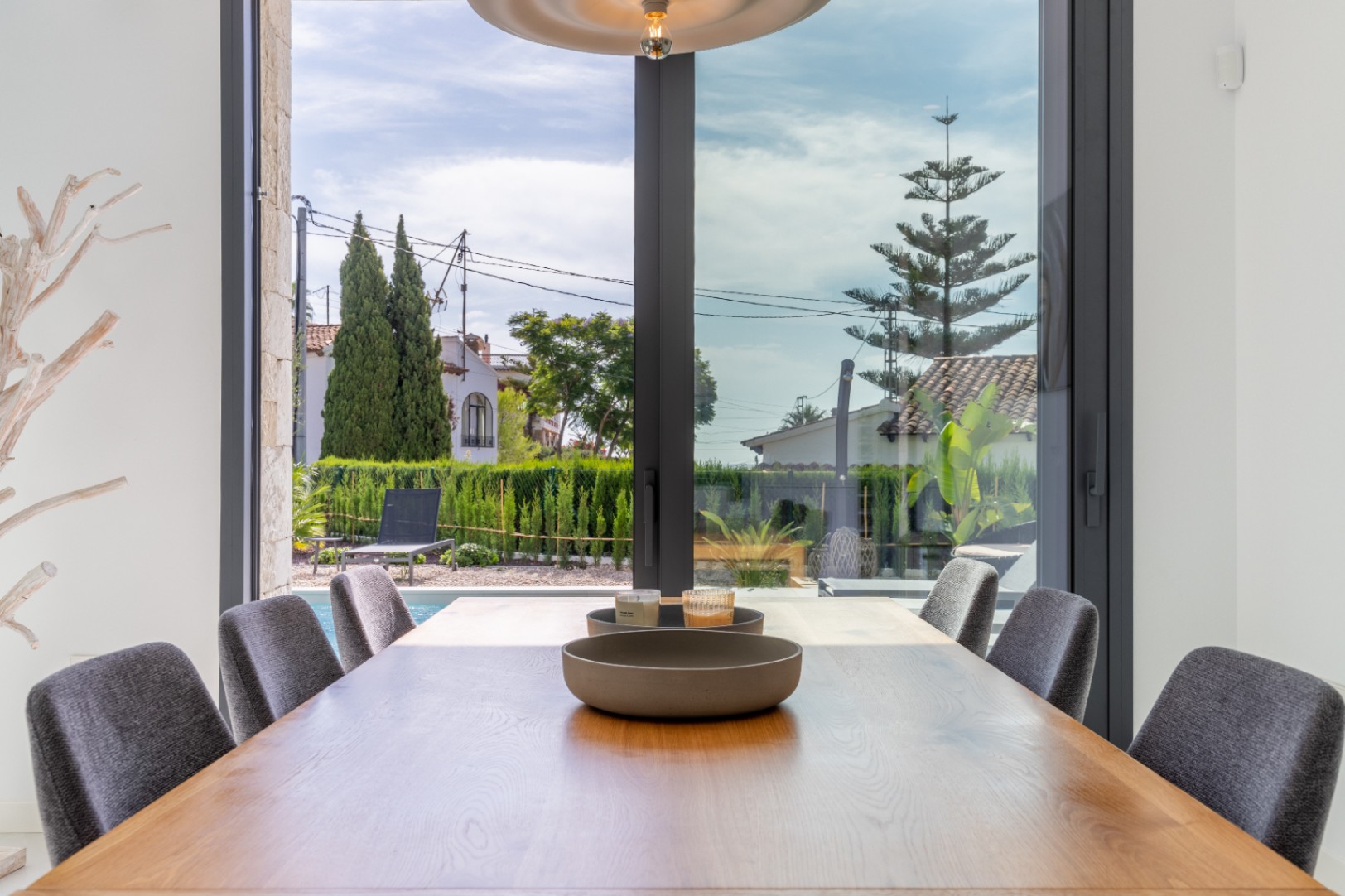 Comedor con mesa de madera y vistas a la piscina y jardín vallado.