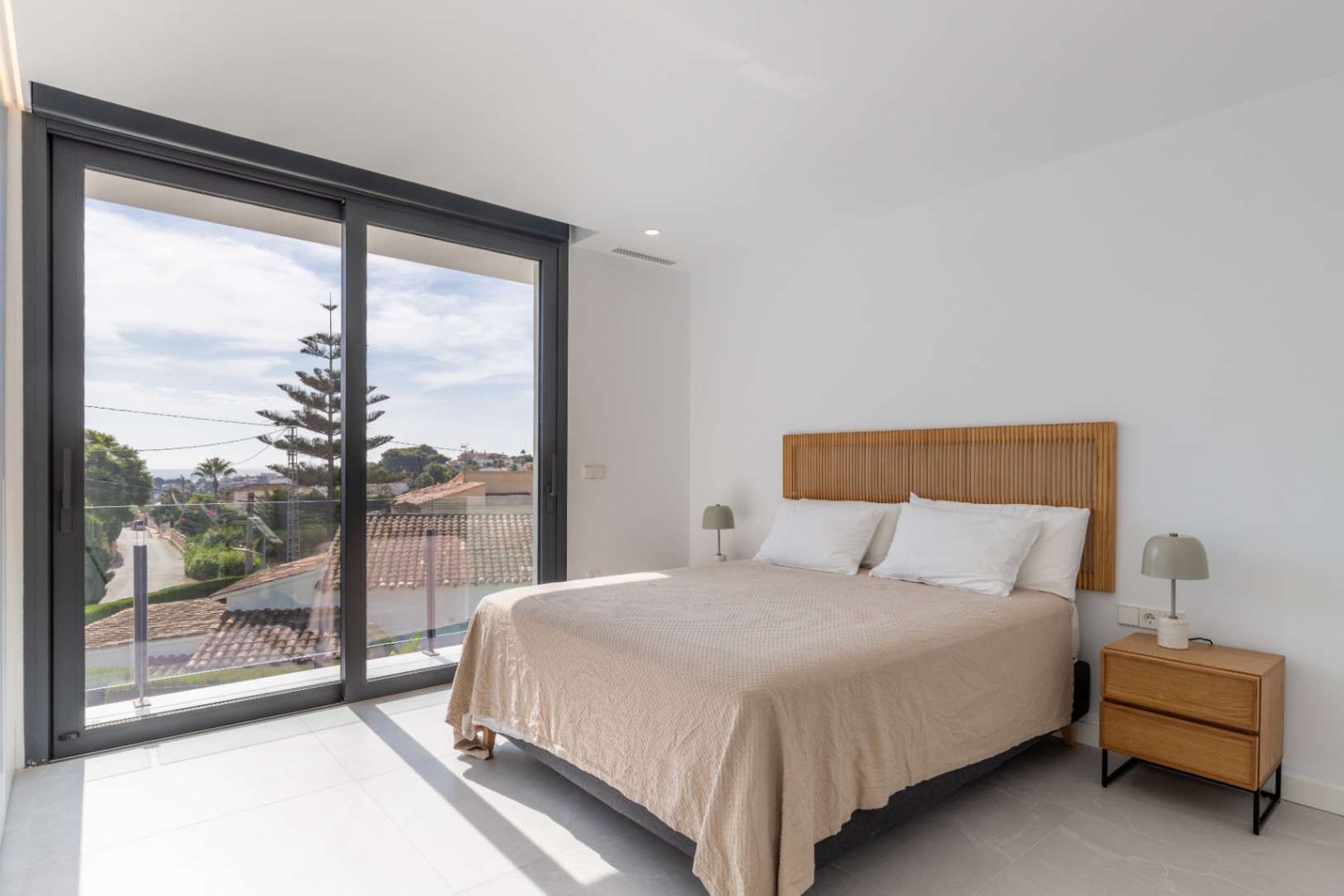 Dormitorio luminoso con cama doble, cabecero de madera y vistas al exterior.