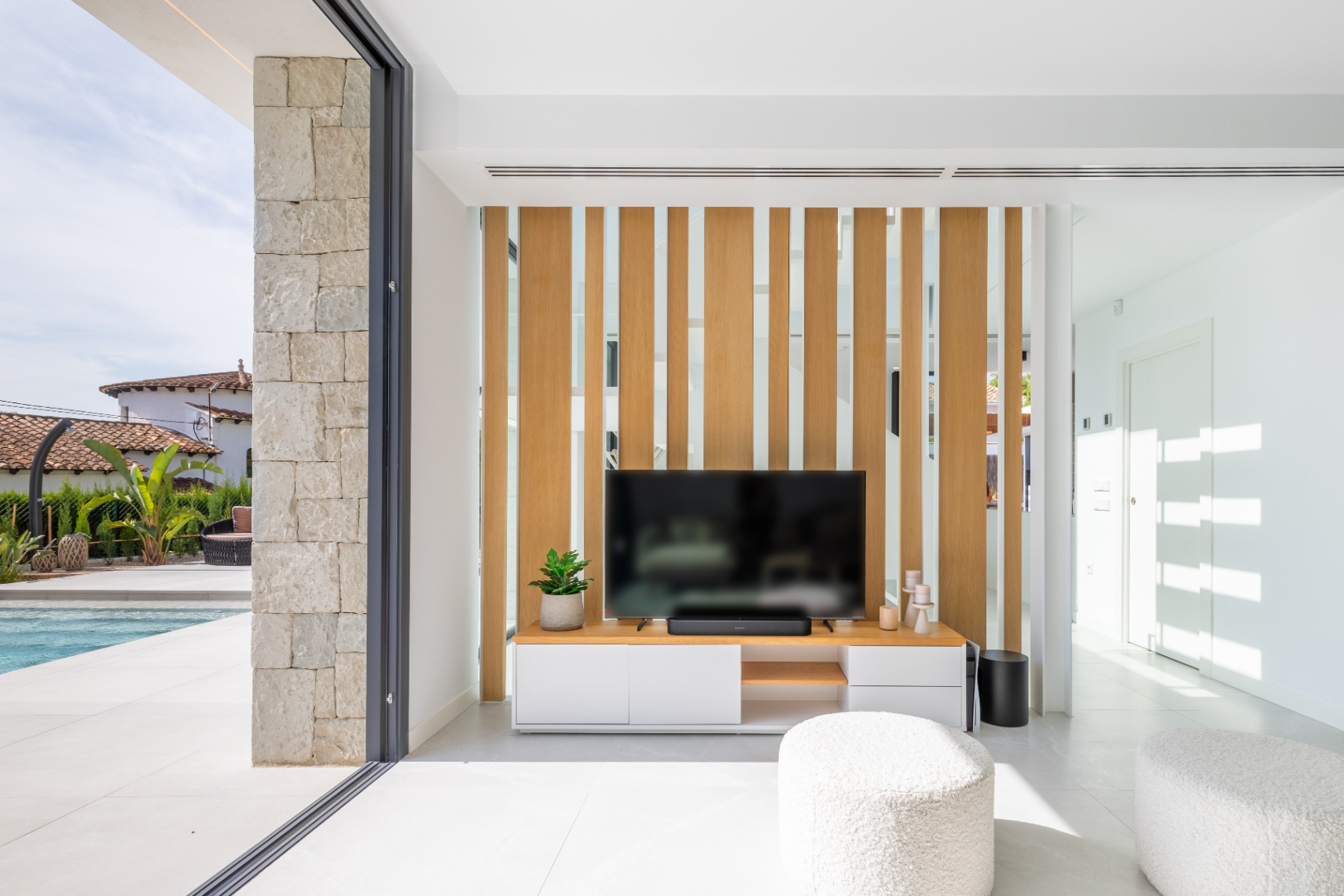 Salón moderno con mueble de TV y celosía de madera clara. Acceso a la terraza con piscina.