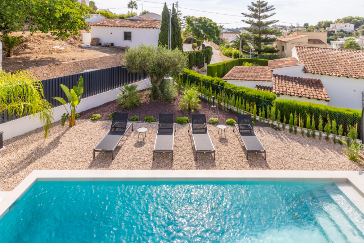 Vista elevada de la piscina con tumbonas, gravilla y jardín con setos en Benissa.