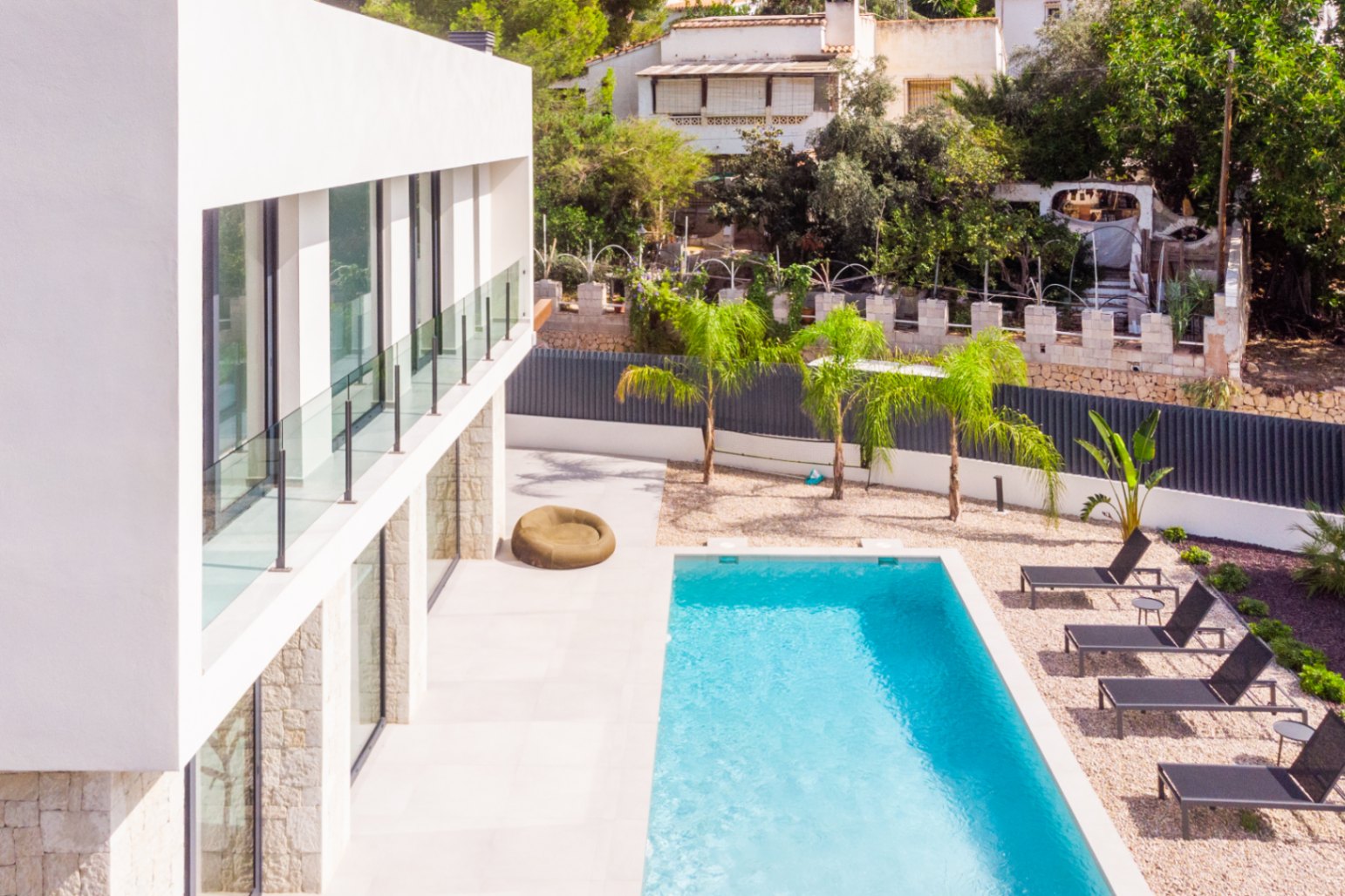 Vista elevada de la piscina privada con tumbonas y jardín de grava con palmeras jóvenes.