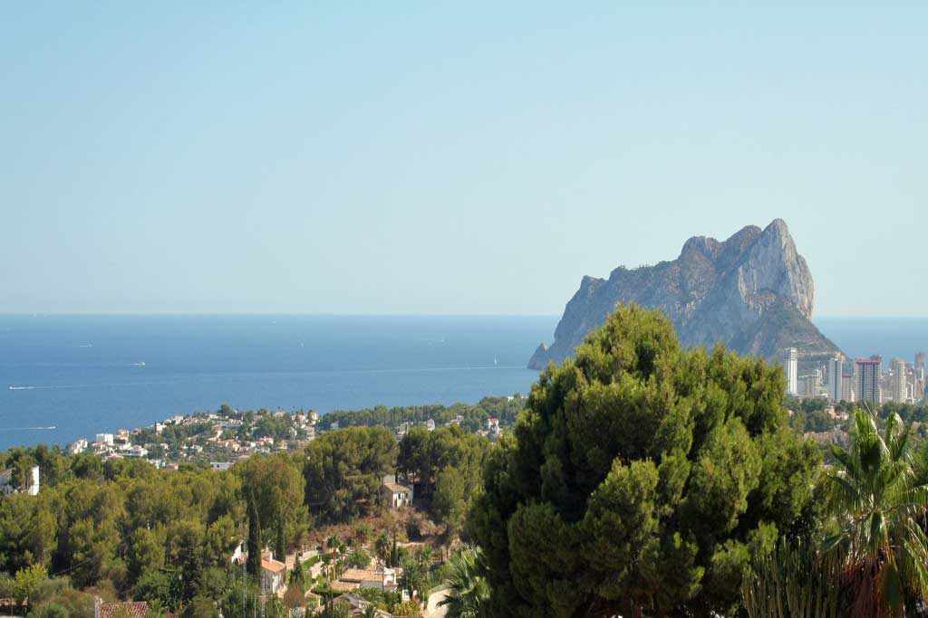 Vistas panorámicas al Mar Mediterráneo y al Peñón de Ifach desde la ubicación elevada de la villa, rodeada de una densa vegetación de pinos.