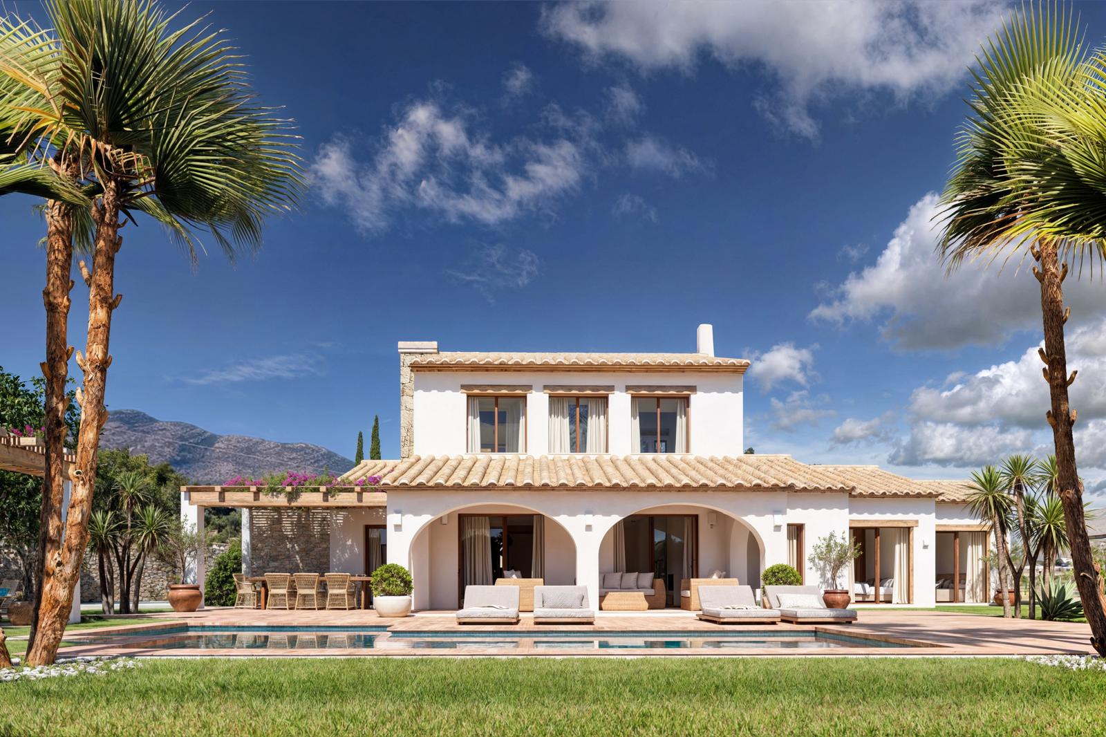 Fachada principal de la villa con porche de arcos, piscina rectangular y solárium de terracota, enmarcada por palmeras y vistas a las montañas bajo un cielo despejado.