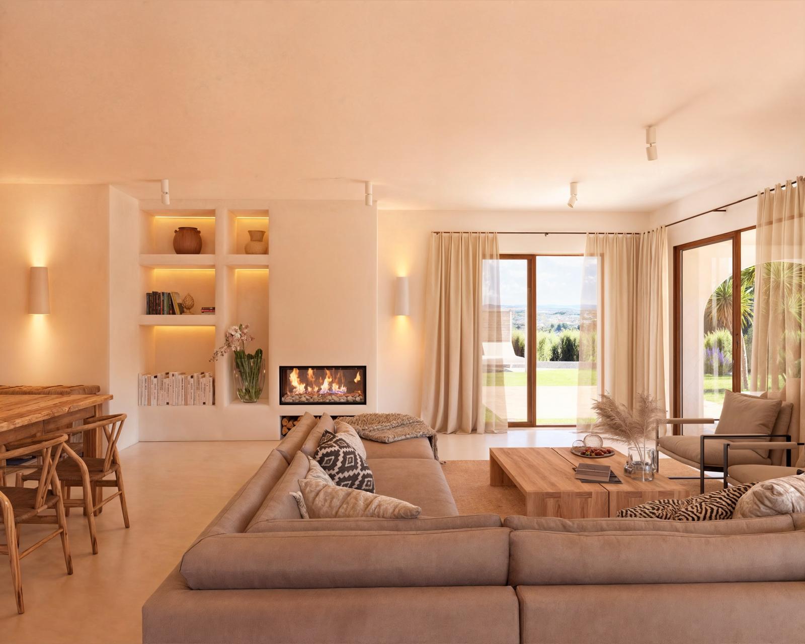 Salón de concepto abierto con chimenea integrada, estanterías retroiluminadas y grandes ventanales Technal que conectan con el jardín y ofrecen luz natural.