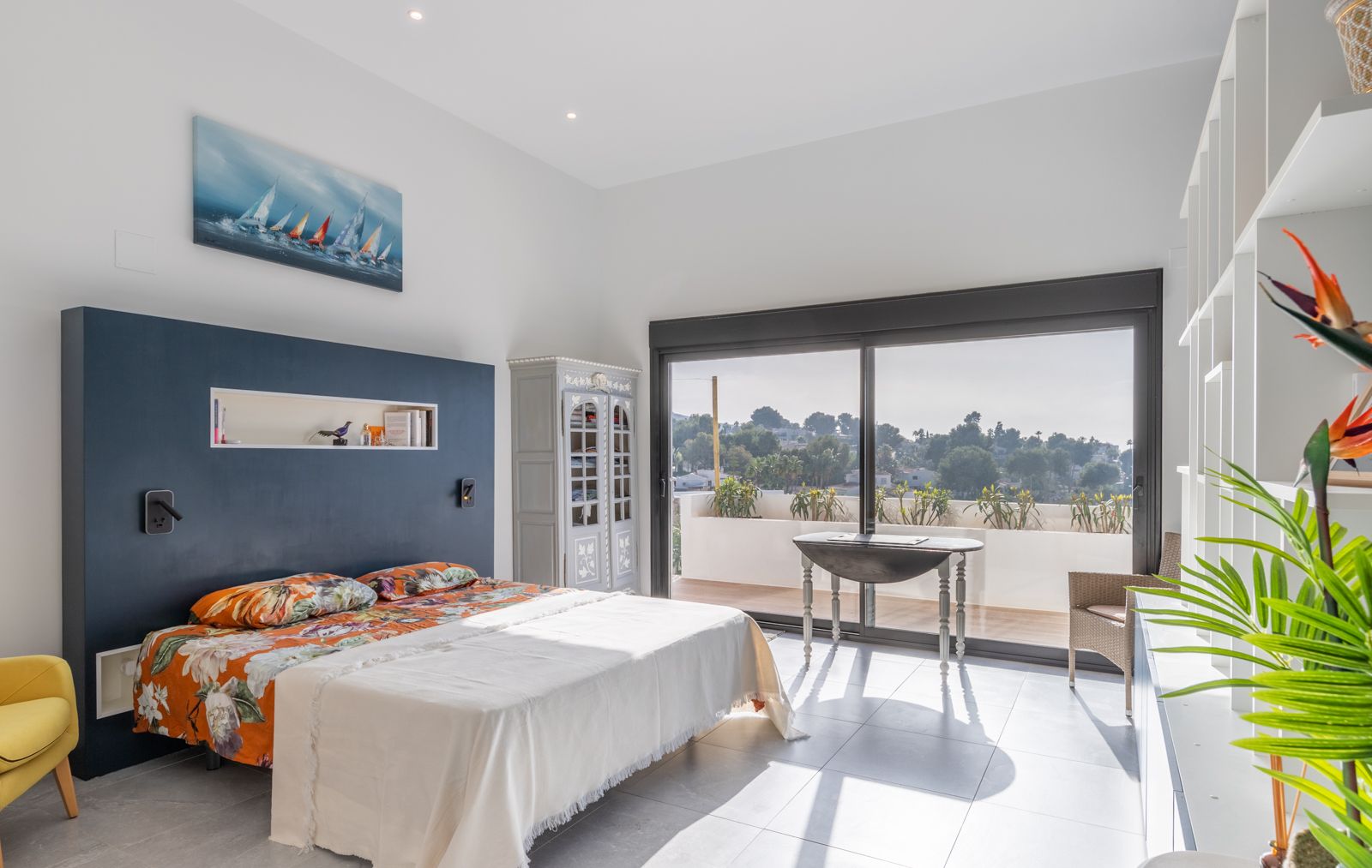 Dormitorio moderno con cabecero azul marino, estantería integrada y acceso directo a una terraza privada mediante grandes ventanales correderos.