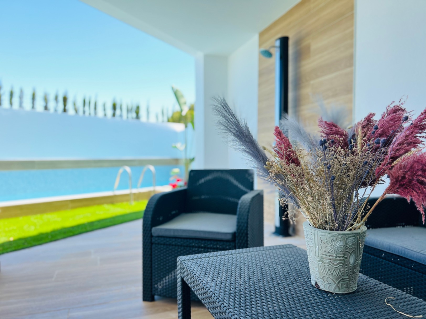 Terraza cubierta con mobiliario de ratán sintético oscuro, zona de estar sombreada y vistas directas a la piscina y el jardín mediterráneo.