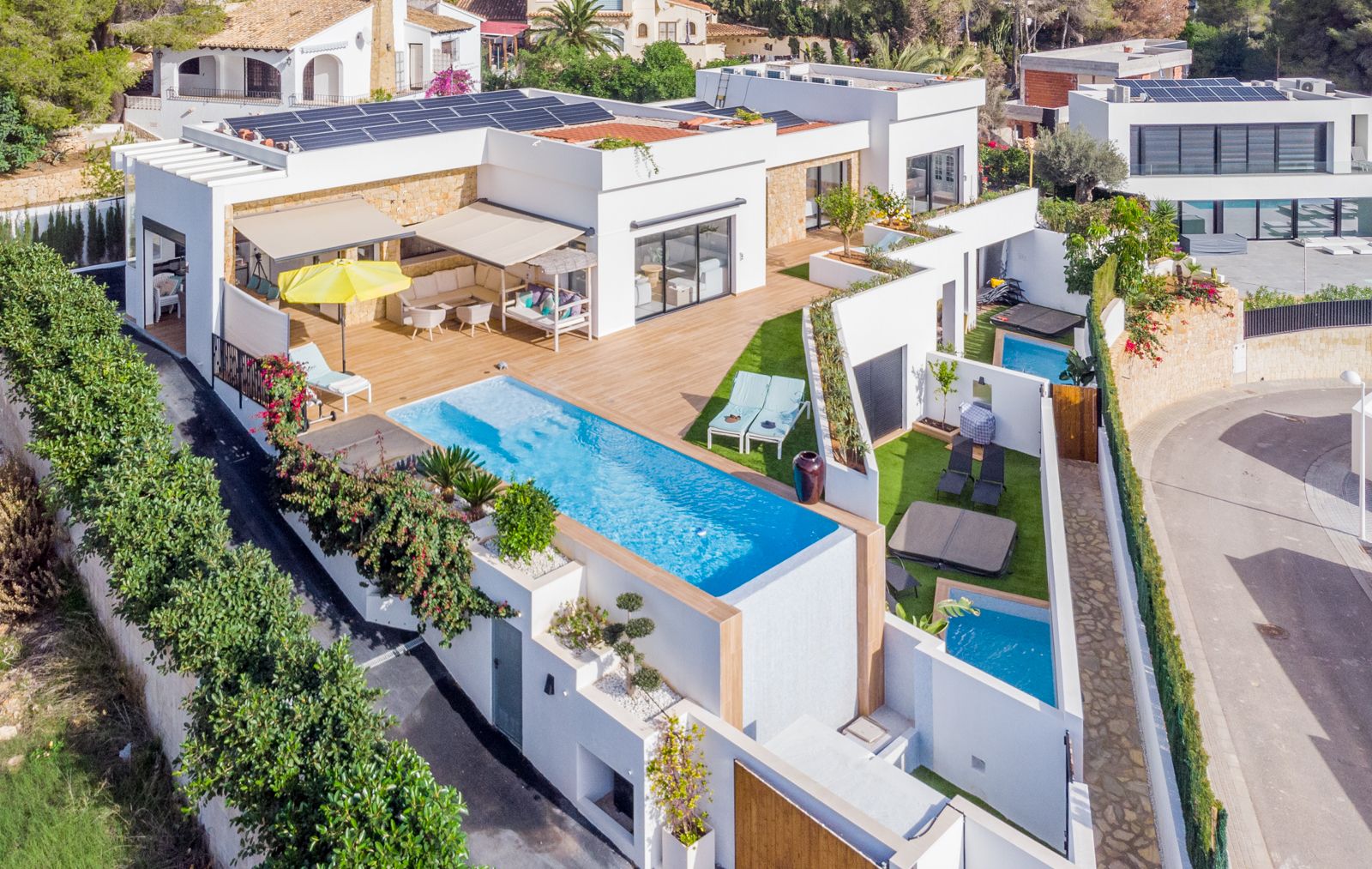 Vista aérea de la villa moderna con piscina infinita, amplias terrazas de madera, paneles solares en el tejado y zonas exteriores privadas para invitados.