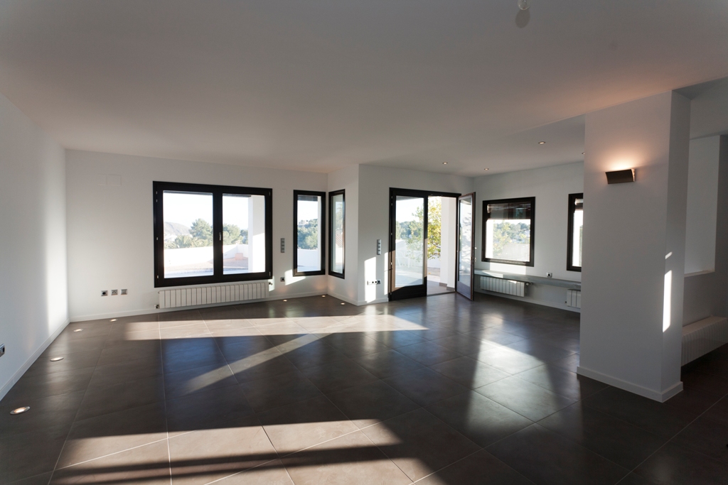 Amplio salón-comedor con suelos de gres oscuro, iluminación integrada en el suelo y grandes ventanales que ofrecen abundante luz natural y acceso directo al exterior.