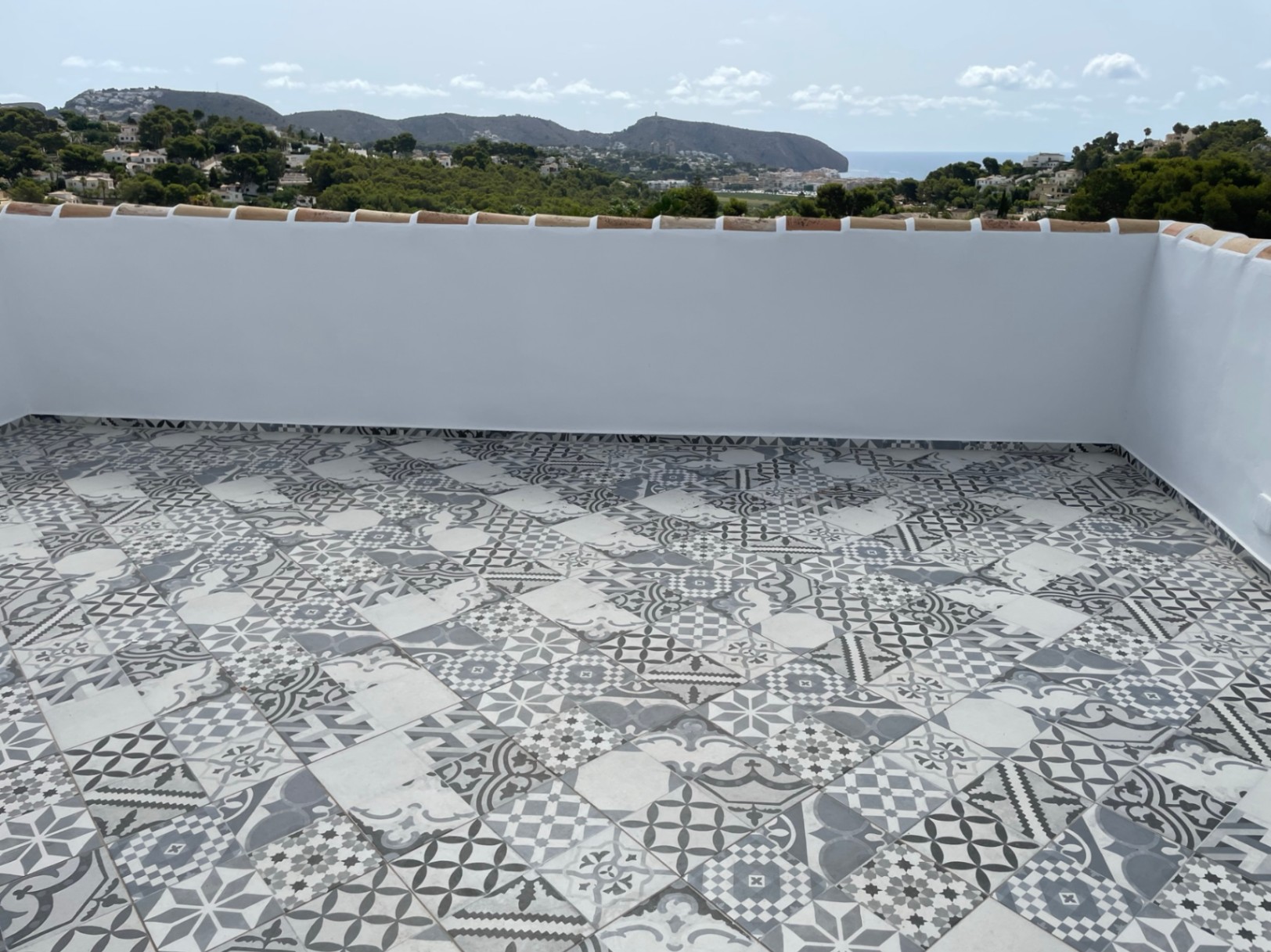 Terraza solárium con suelo de baldosas hidráulicas decorativas y vistas panorámicas al mar Mediterráneo y la costa de Moraira.
