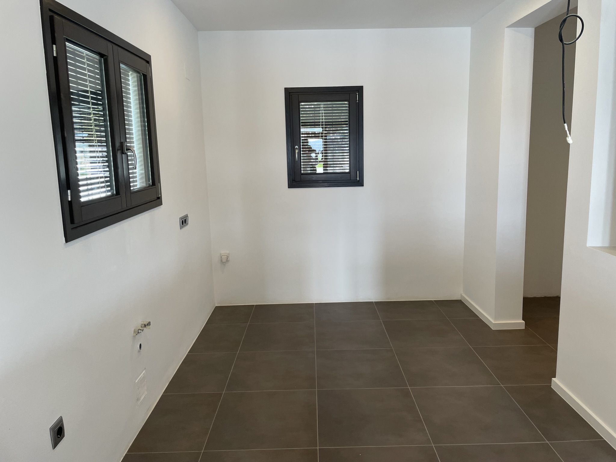 Zona interior con preinstalaciones de fontanería y electricidad, suelos de gres porcelánico oscuro y ventanas de aluminio con persianas integradas.