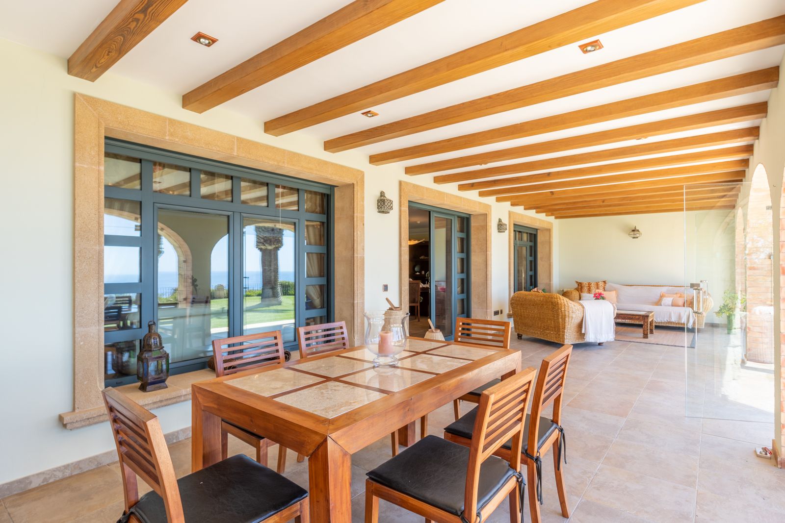 Comedor exterior cubierto con vigas de madera y vistas al jardín y al mar.