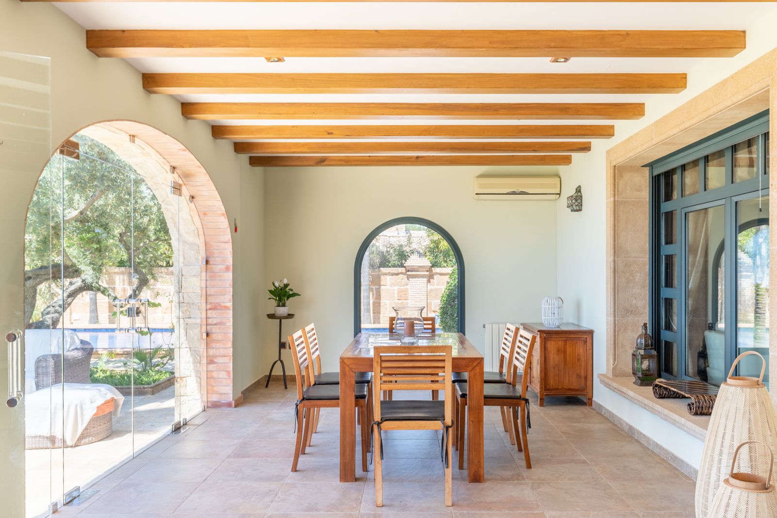 Comedor luminoso con mesa de madera y acceso al jardín y piscina a través de arcos de ladrillo.