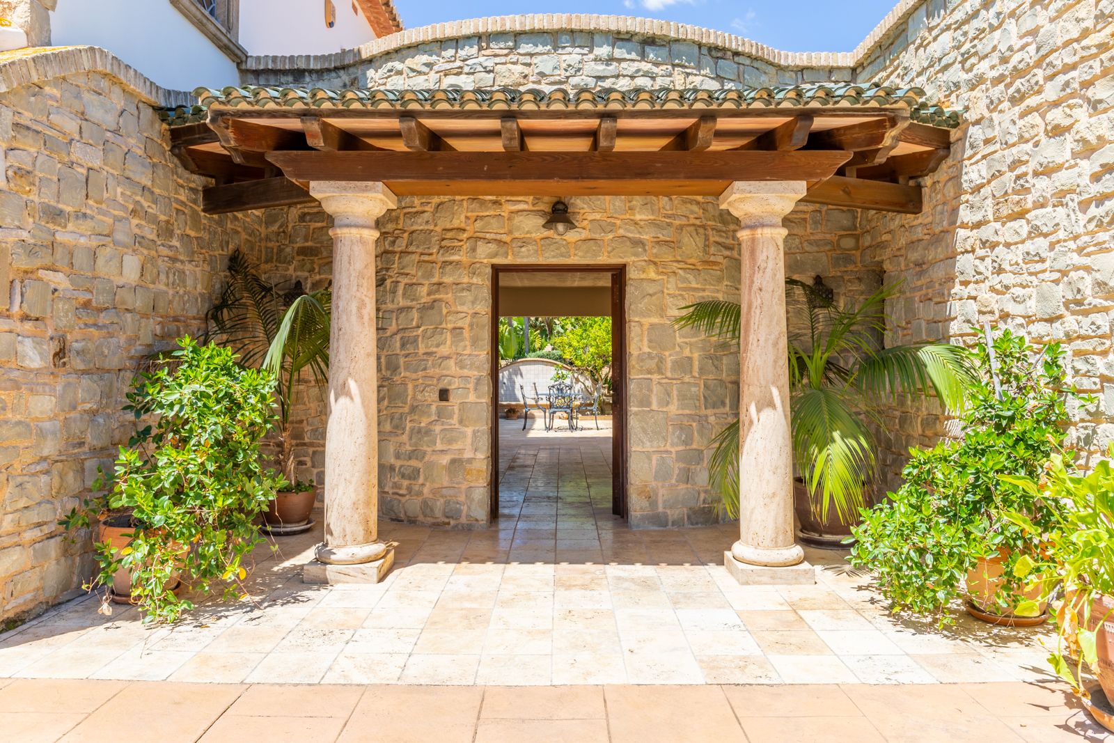 Entrada porticada con columnas de piedra y vegetación exuberante.