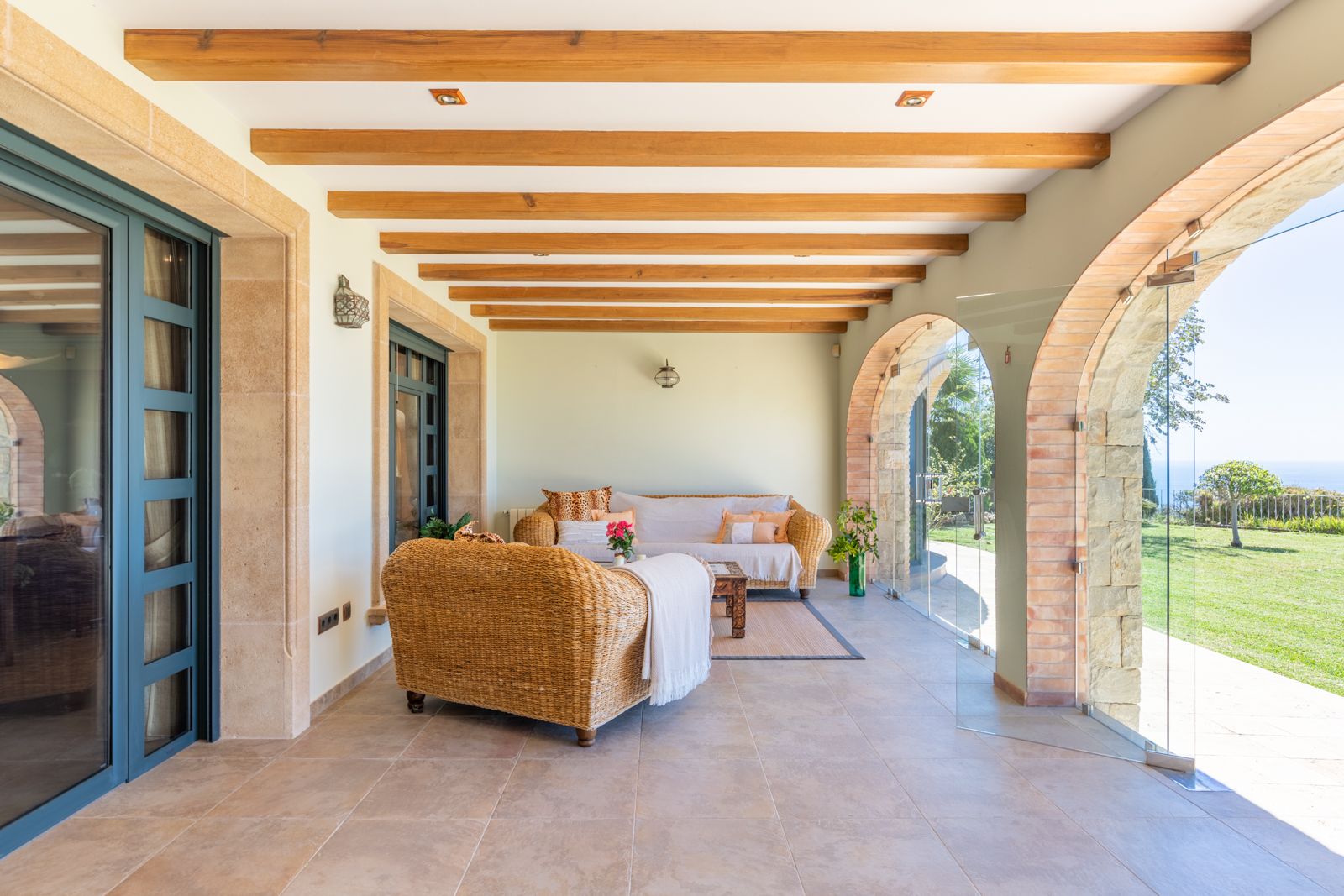 Porche con vigas de madera, arcos de piedra y vistas al jardín y al mar.
