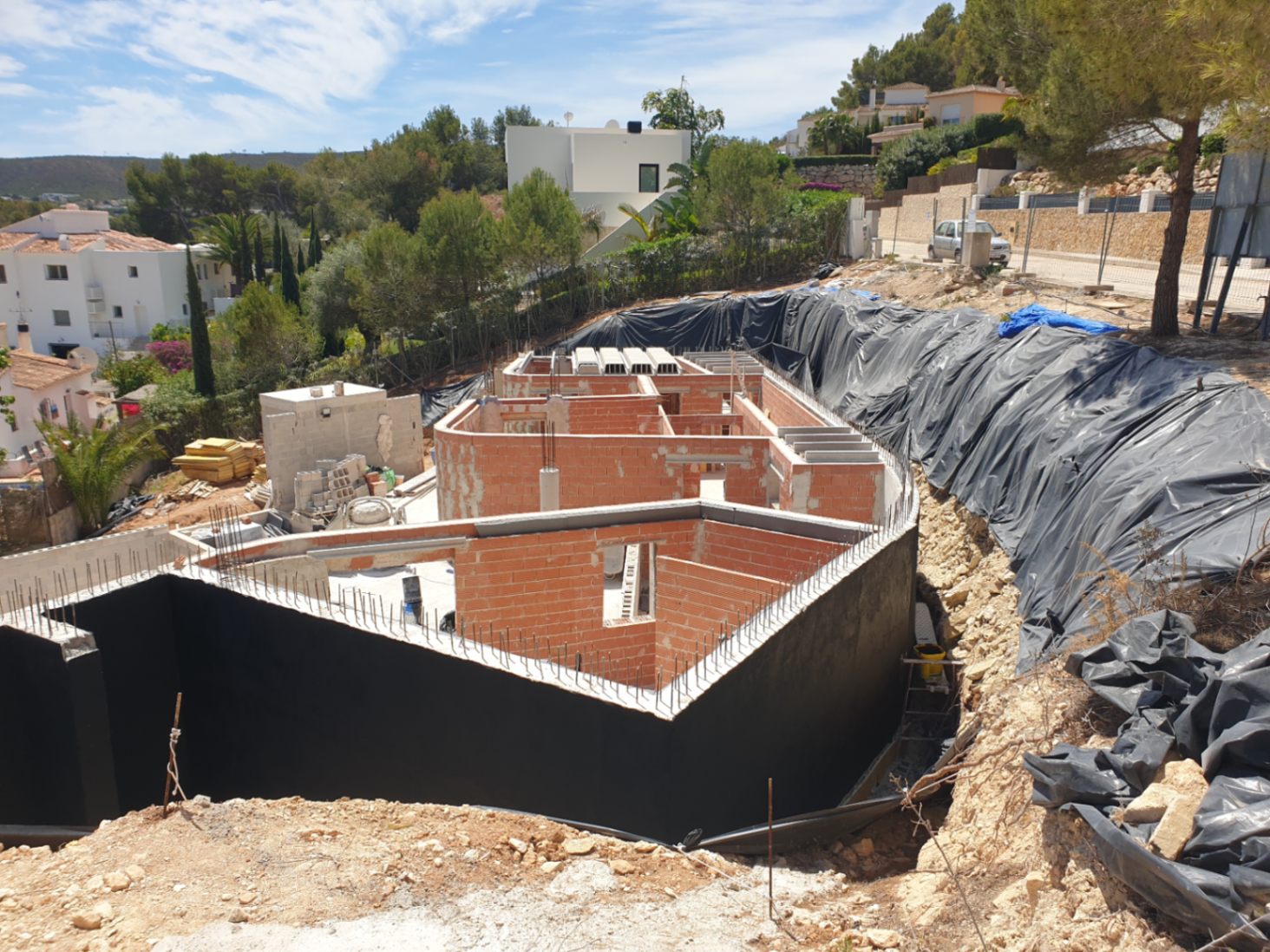 Estado actual de la construcción mostrando la estructura de ladrillo y muros de contención impermeabilizados en una parcela elevada con vistas despejadas.