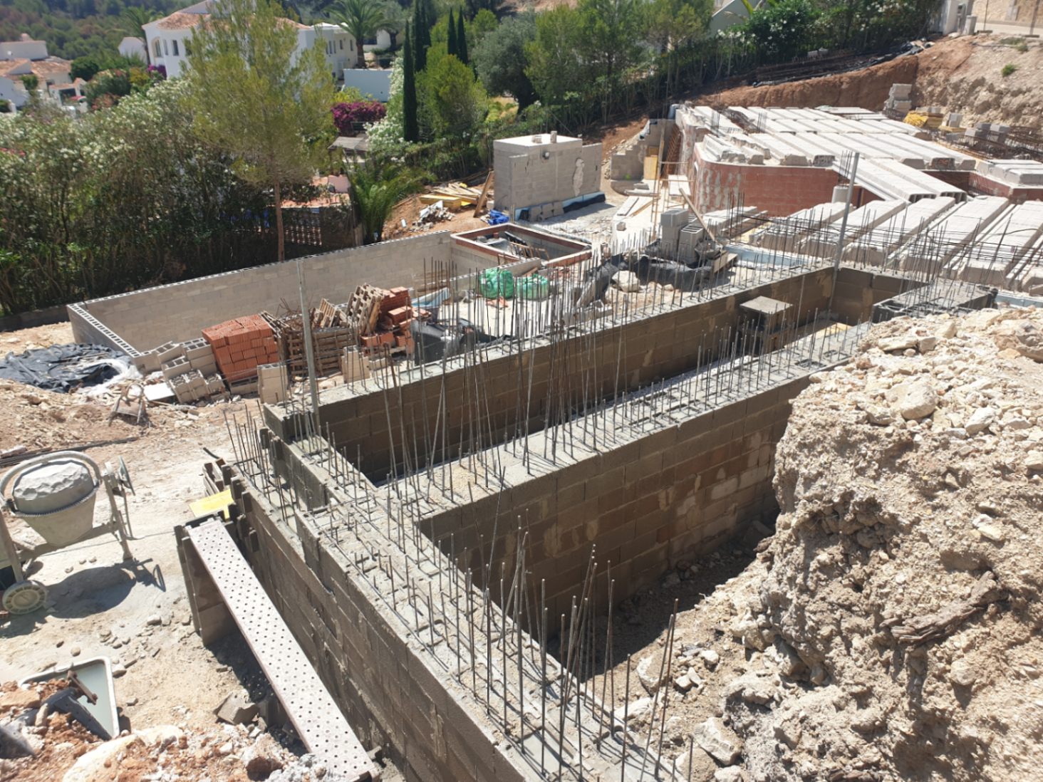 Fase inicial de construcción que muestra los muros de cimentación con armadura de acero y bloques de hormigón en una parcela elevada con entorno natural.