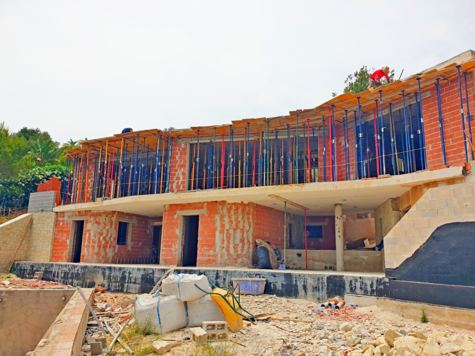 Vista exterior de la villa en fase de construcción, mostrando la estructura de ladrillo cerámico, forjados de hormigón y la curvatura arquitectónica de la planta superior.
