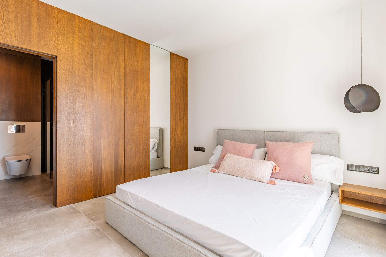 Dormitorio con armarios de roble a medida, suelos de gres porcelánico de gran formato y acceso directo a un baño en suite con acabados de mármol.
