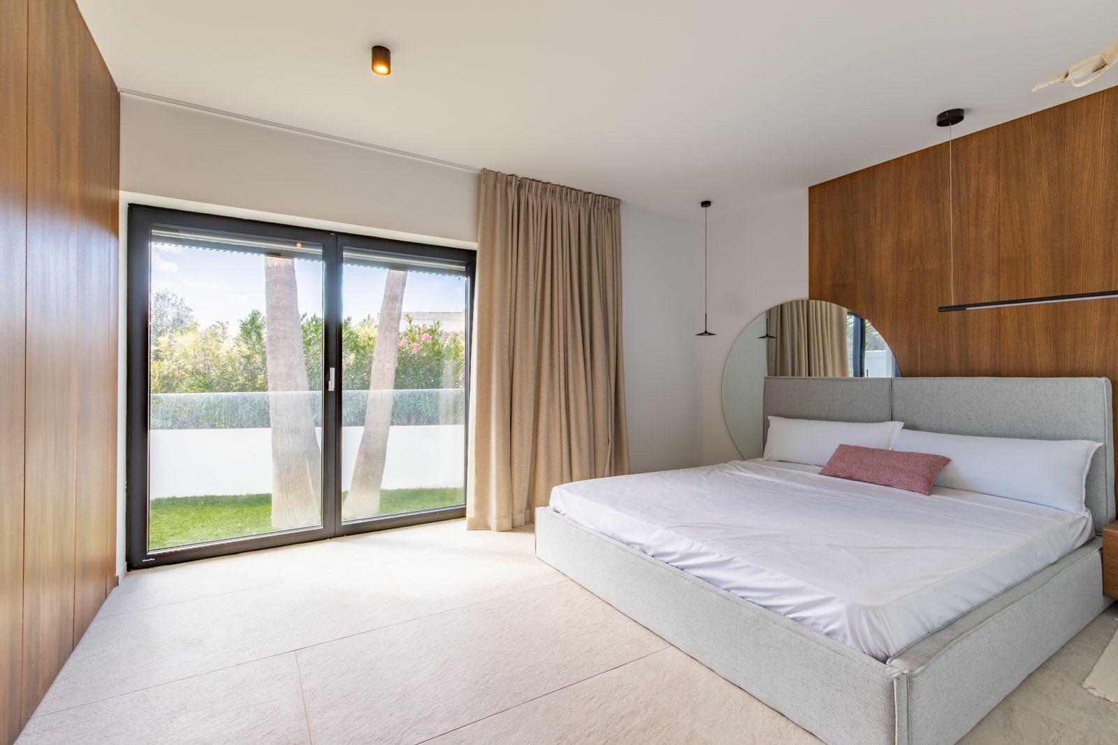 Dormitorio con paneles de roble natural, suelos de gres porcelánico y acceso directo al jardín mediante ventanales de triple acristalamiento.