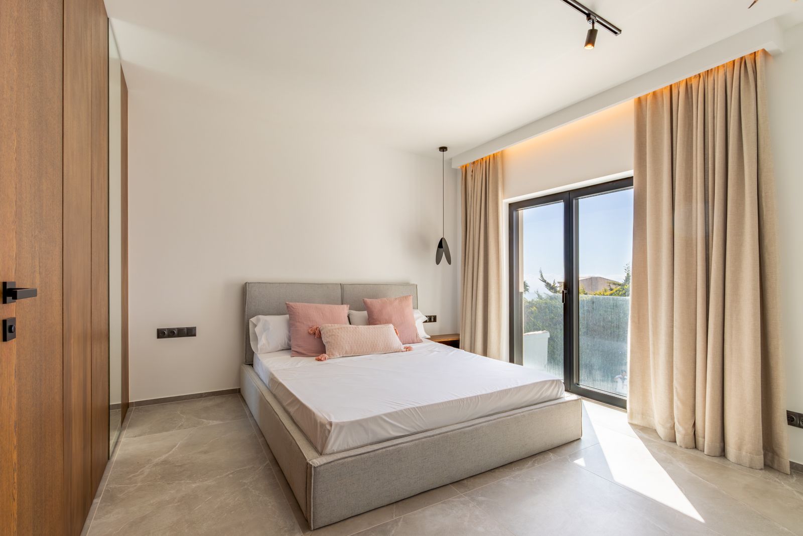 Dormitorio moderno con suelos de gres porcelánico, carpintería de roble a medida con espejo integrado y acceso directo al exterior mediante ventanales de gran formato.