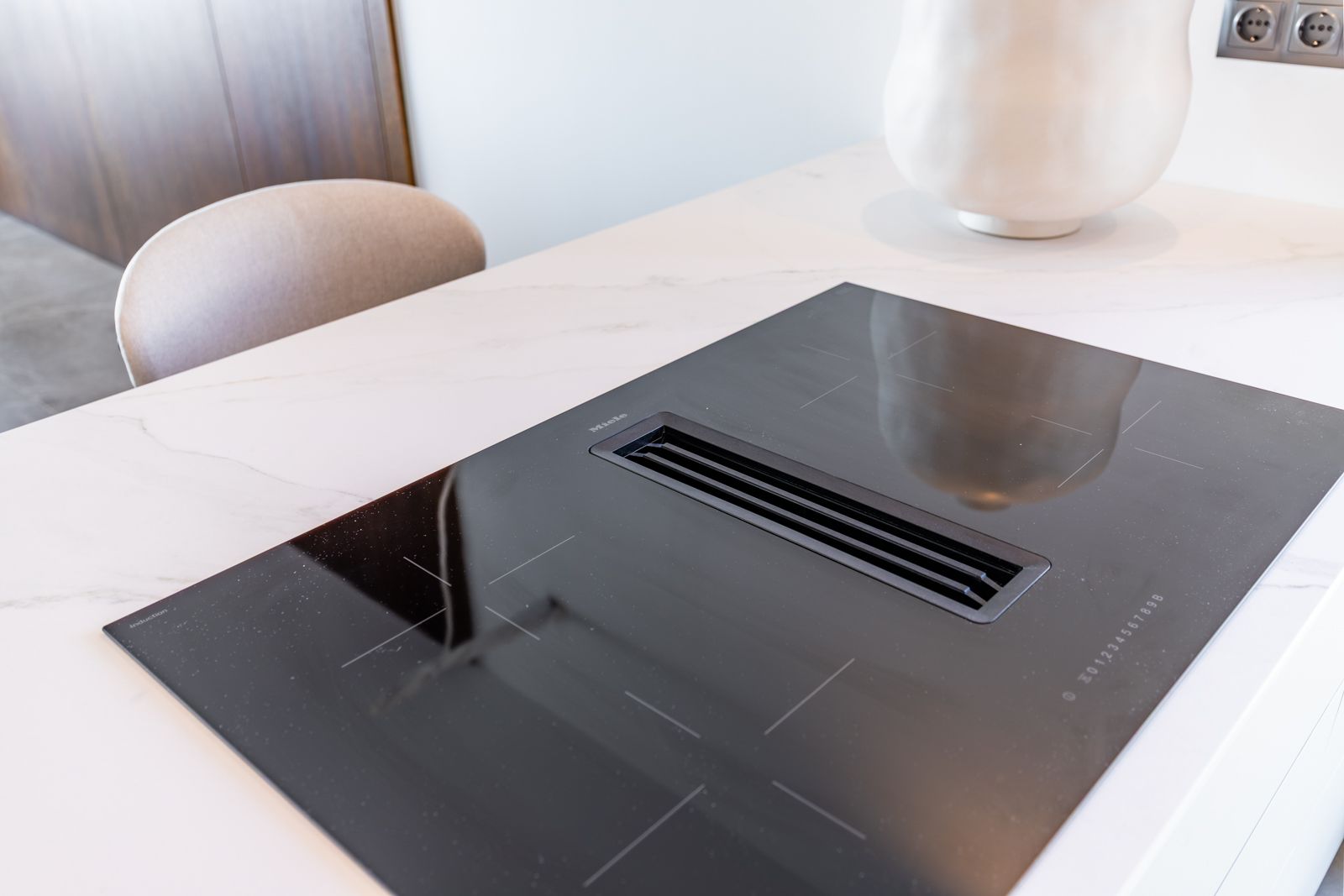 Placa de inducción Miele con extractor integrado sobre encimera de piedra sinterizada blanca con veteado gris.