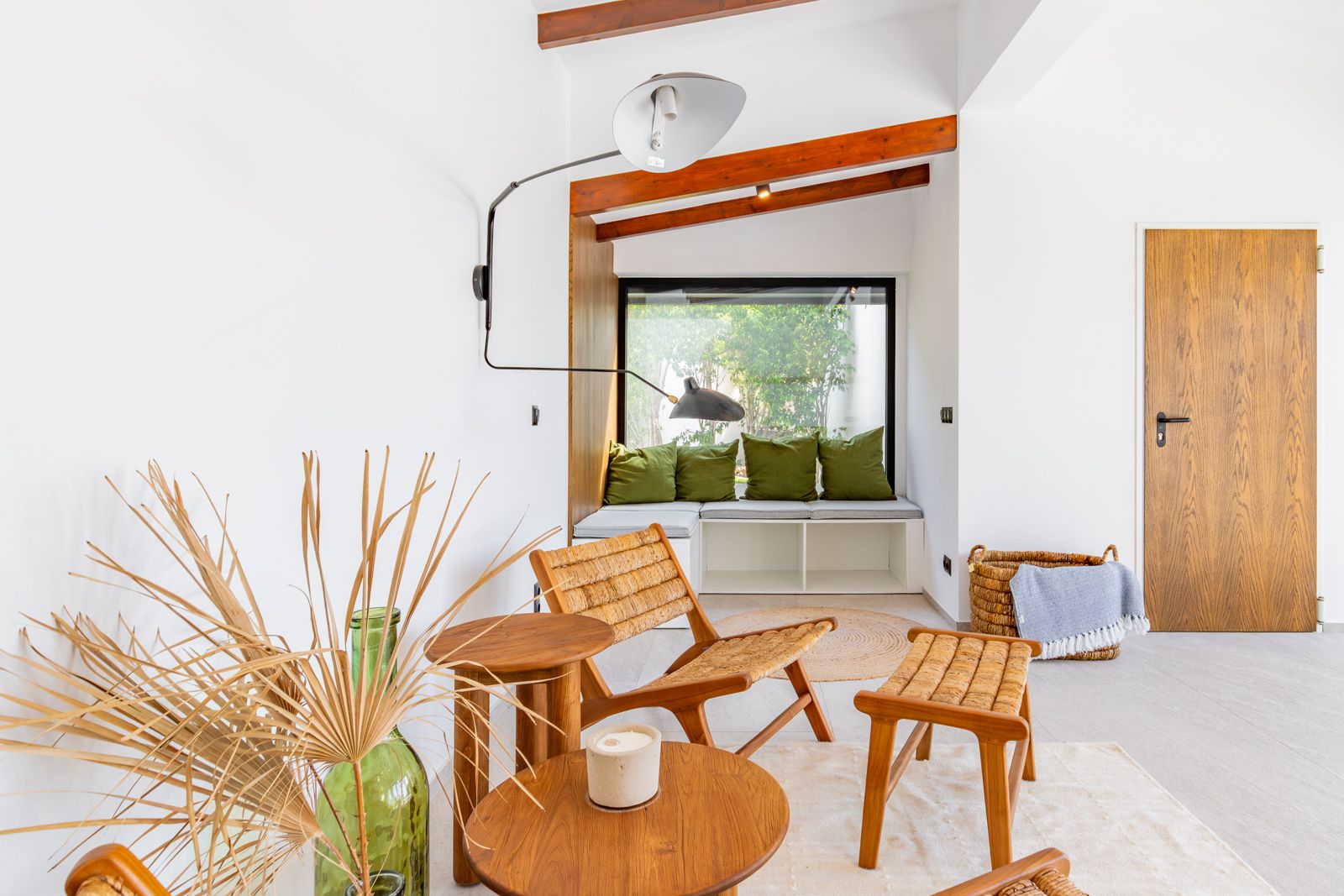 Rincón de lectura con banco integrado bajo ventanal, vigas de madera vista y mobiliario de fibras naturales. Destaca la puerta de roble y la iluminación técnica de diseño.