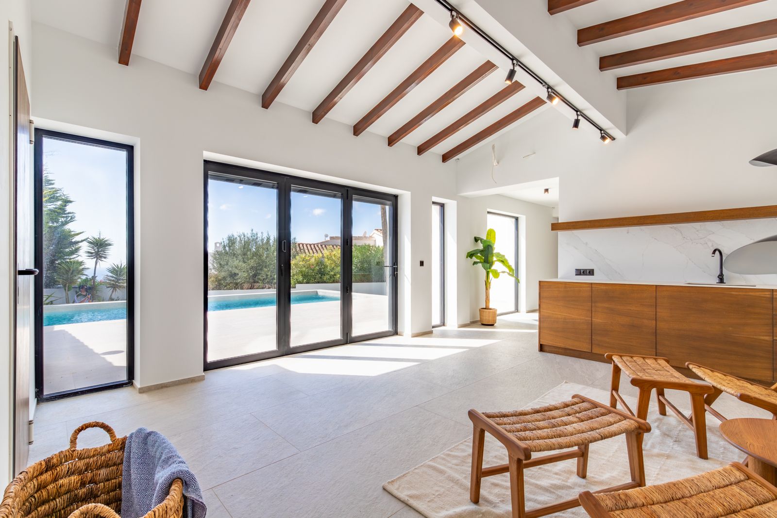 Salón diáfano con vigas de madera vista, suelos de gres porcelánico y ventanales de gran formato con acceso directo a la terraza y piscina privada.