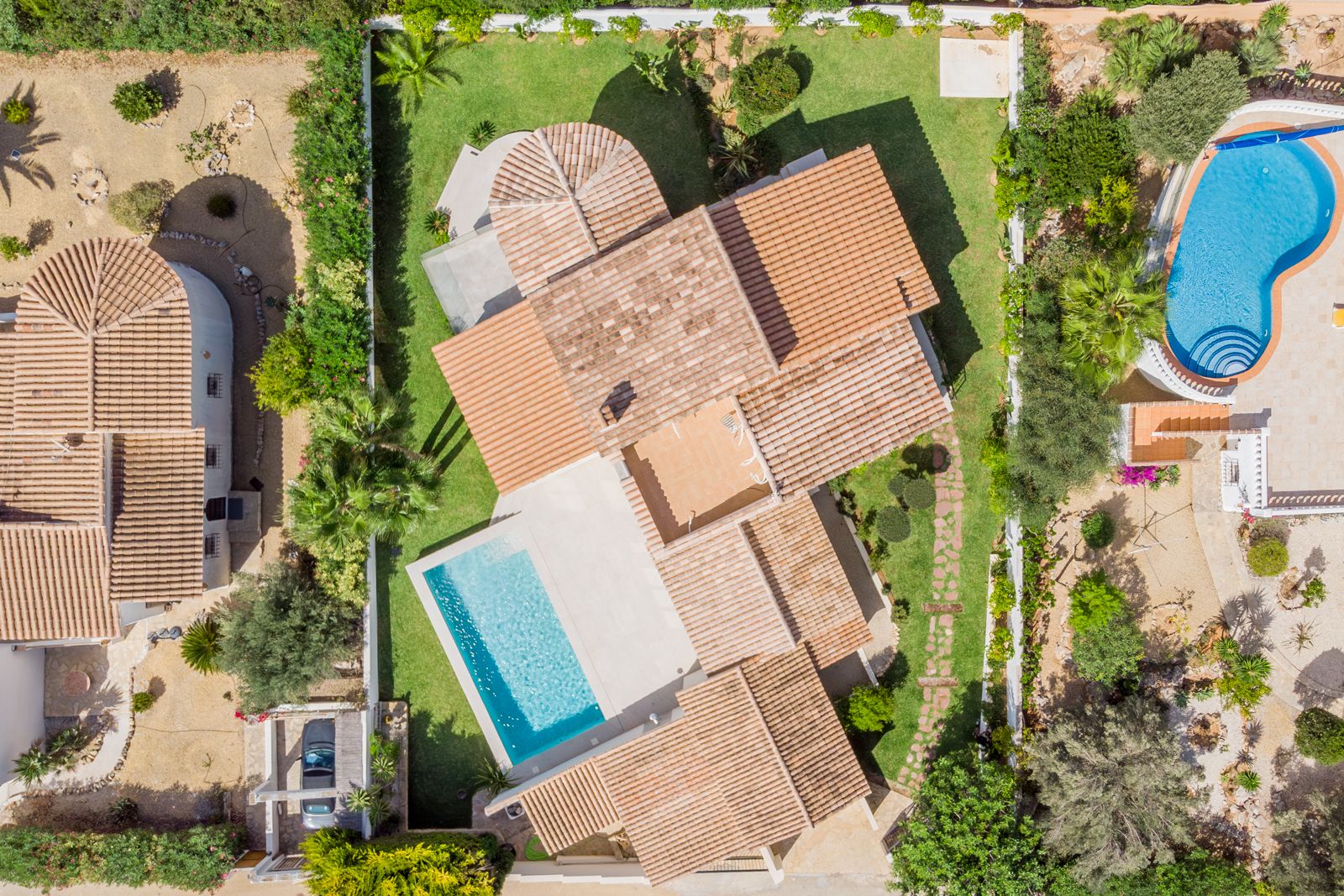 Vista aérea cenital de la villa que muestra la distribución de los tejados de teja cerámica, la piscina rectangular y el jardín perimetral con césped cuidado.