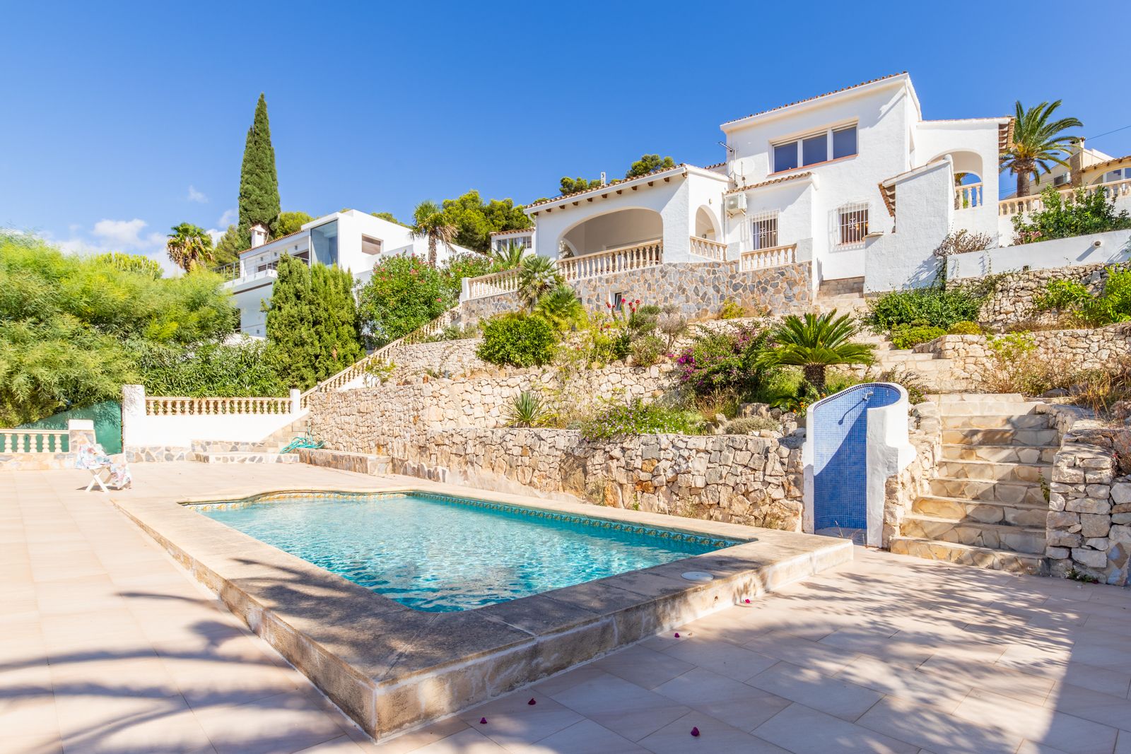 Piscina privada rodeada de una amplia terraza soleada, con muros de piedra natural y jardines abancalados que conducen a la villa de estilo mediterráneo.