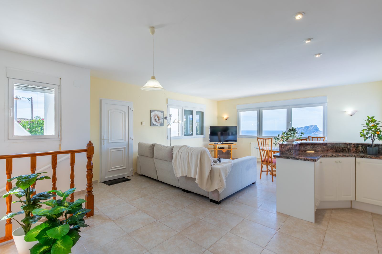 Salón comedor de planta abierta con cocina integrada, encimeras de granito y vistas panorámicas al mar y al Peñón de Ifach a través de amplios ventanales.
