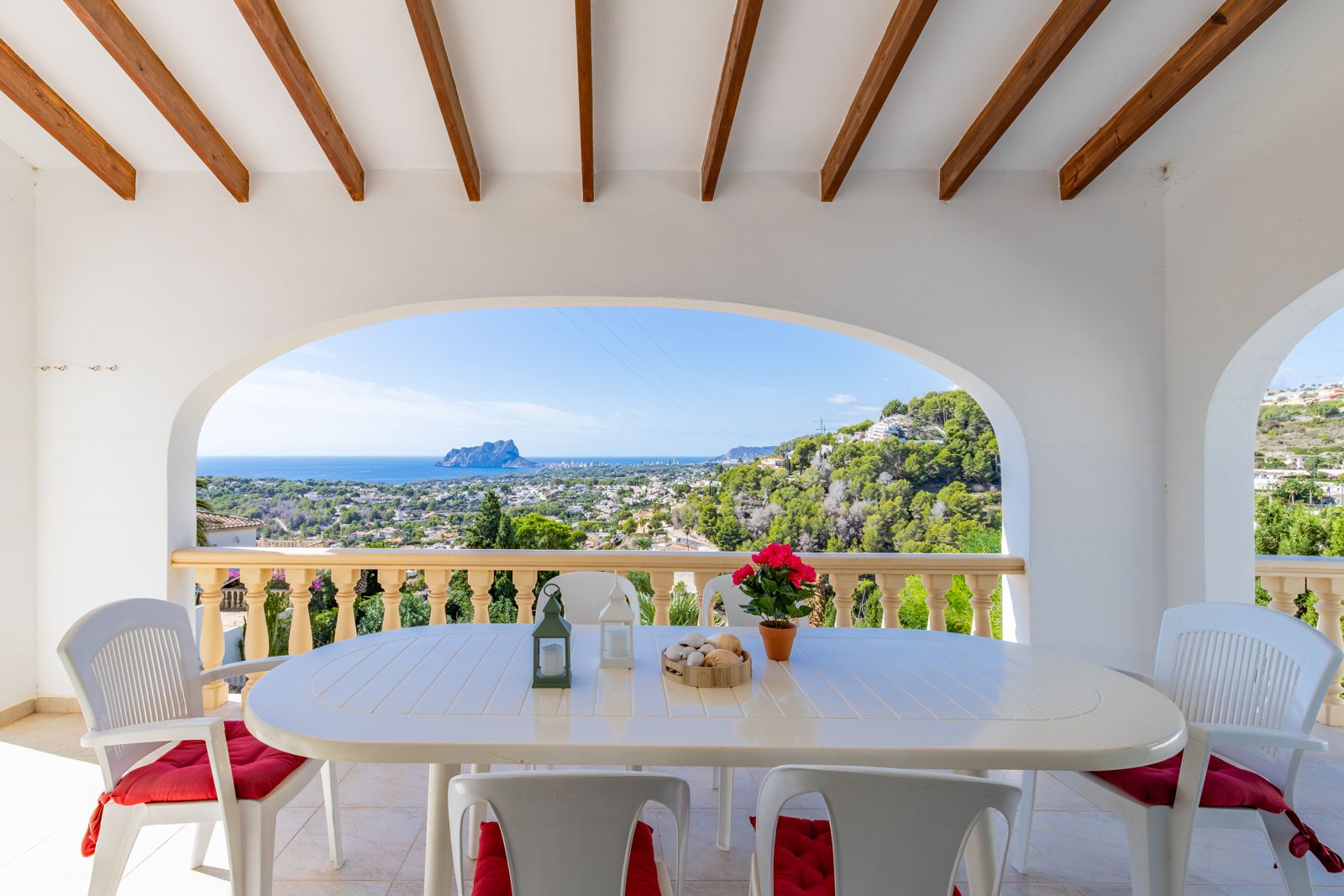 Terraza cubierta con vigas de madera y arcos mediterráneos que ofrece vistas panorámicas al mar y al Peñón de Ifach desde la zona de comedor exterior.