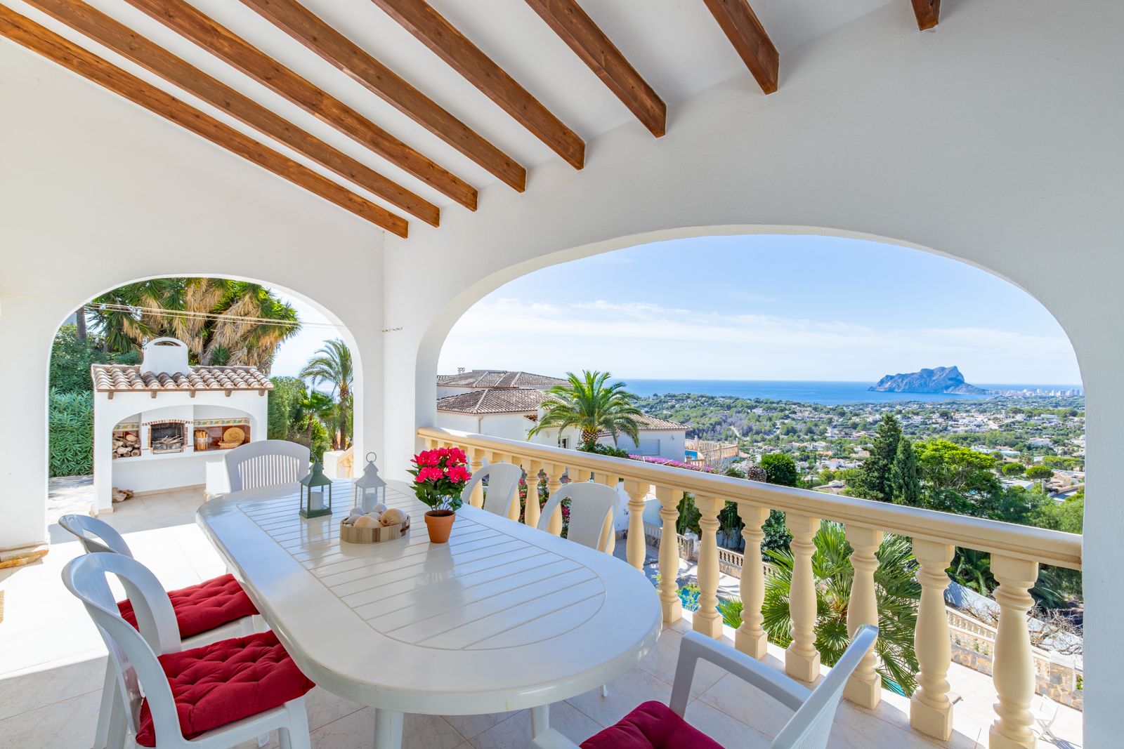 Terraza cubierta con vigas de madera y zona de comedor exterior, ofreciendo vistas panorámicas al mar y al Peñón de Ifach junto a la barbacoa.