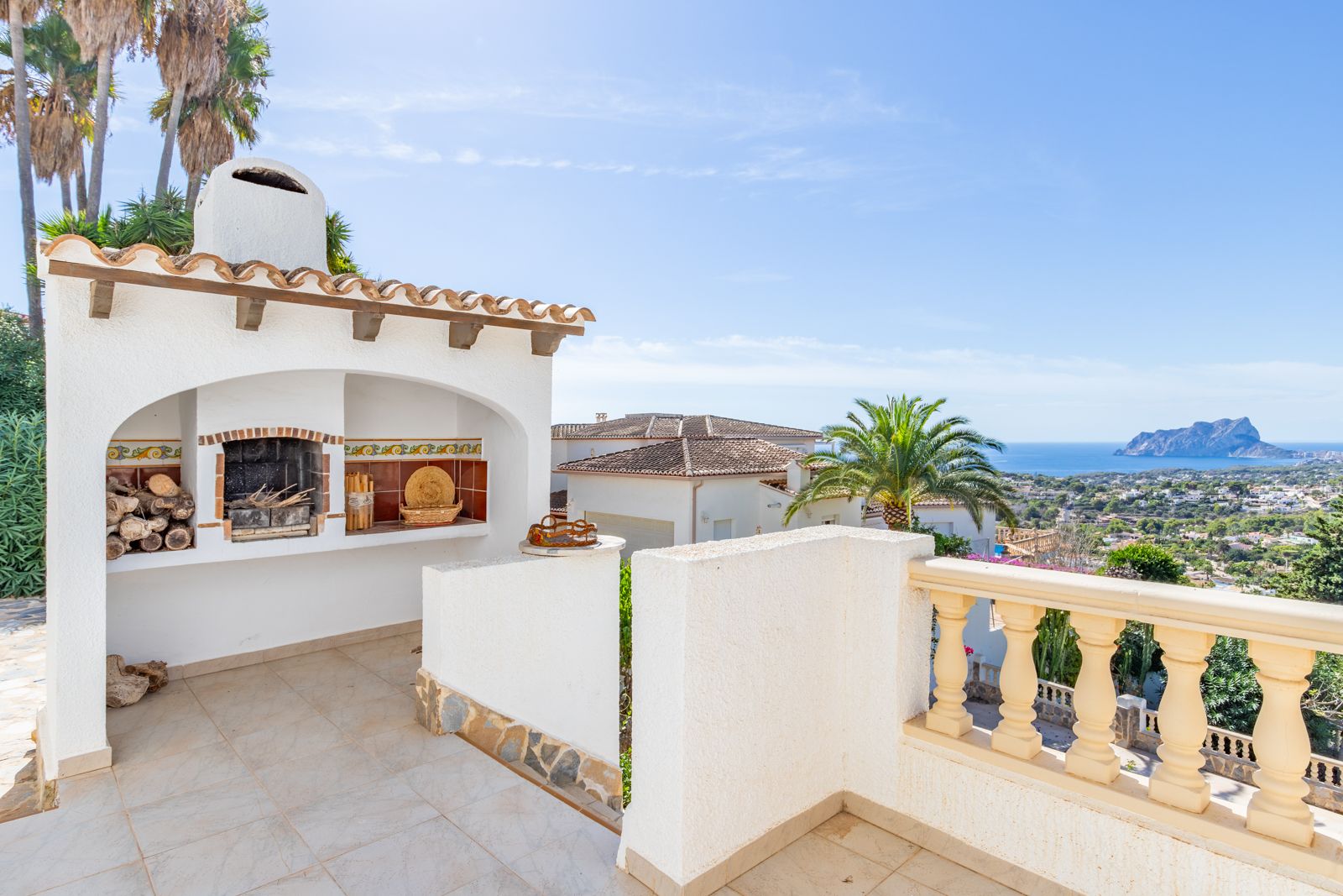Zona de barbacoa de obra con chimenea y detalles cerámicos en la terraza superior, ofreciendo vistas panorámicas al mar y al Peñón de Ifach.