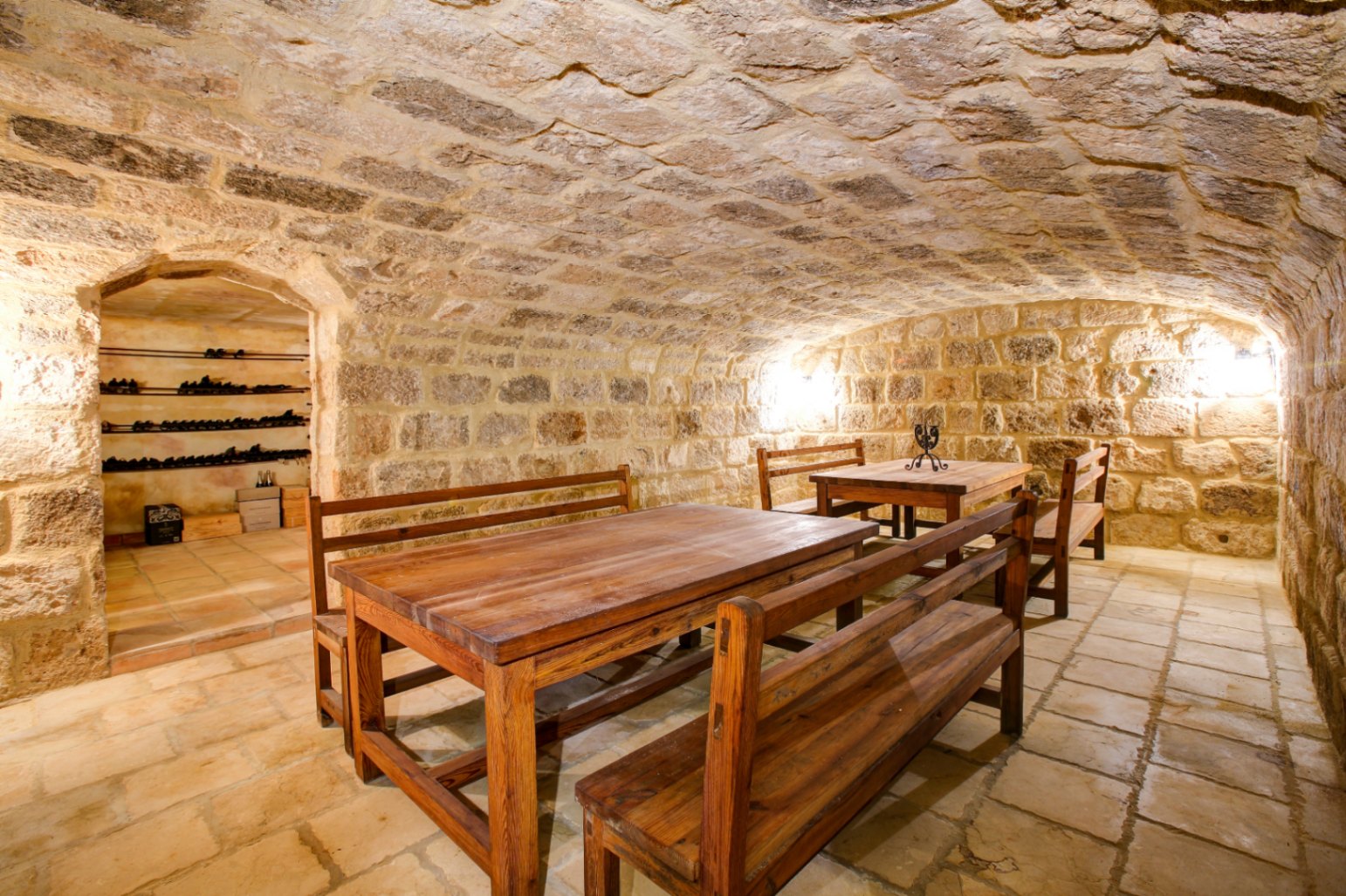 Bodega con techo de bóveda en piedra natural, suelos de barro cocido y mesas de madera maciza, que incluye una zona anexa para la guarda de vinos.