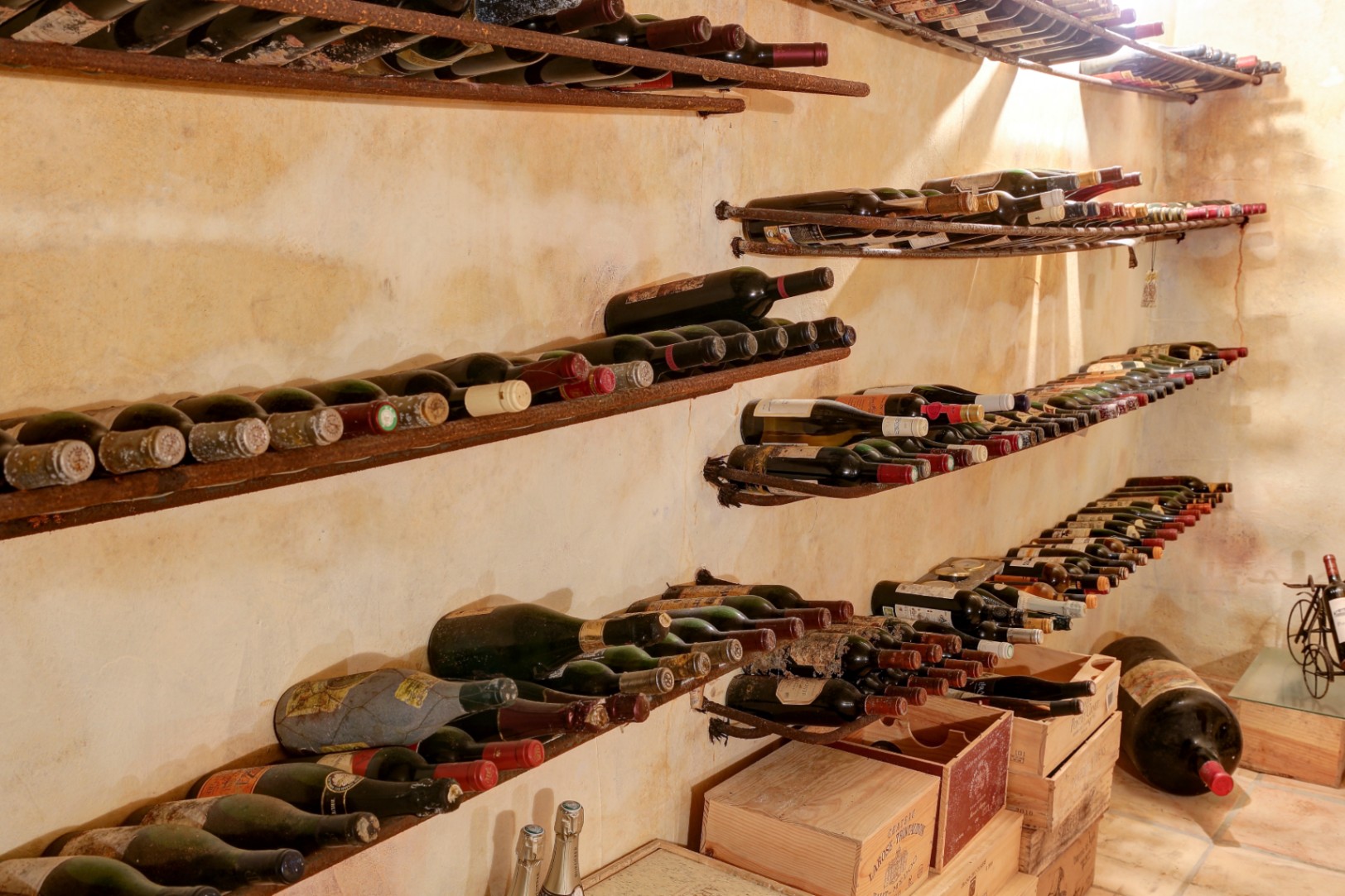 Bodega rústica con paredes de textura envejecida, estanterías metálicas para botellas y cajas de madera originales para el almacenamiento de vinos.