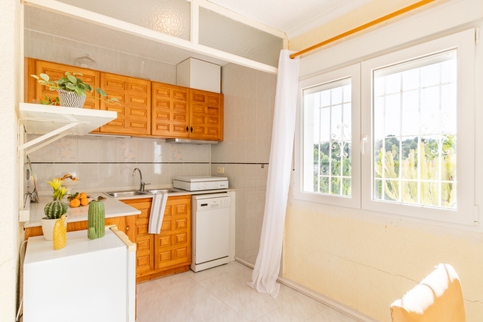 Cocina funcional del apartamento independiente con armarios de madera, encimera blanca y gran ventanal que aporta abundante luz natural.