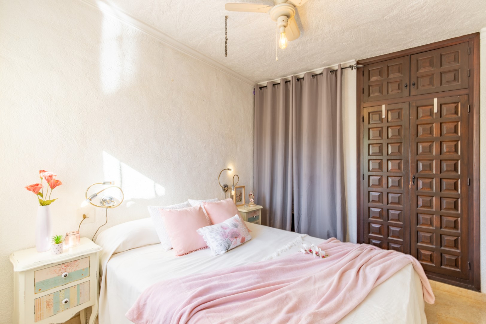 Dormitorio con armario empotrado de madera oscura tallada, paredes de yeso texturizado y ventilador de techo. La estancia recibe abundante luz natural lateral.